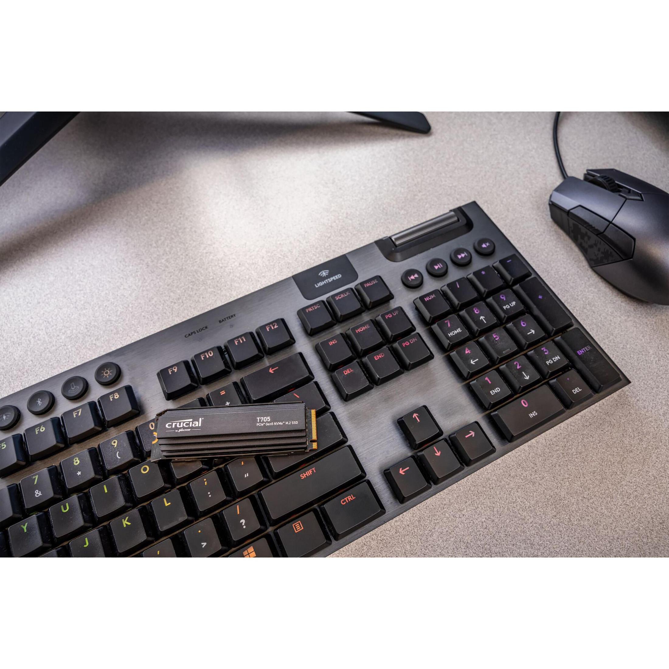 Klawiatura z zainstalowanym dyskiem SSD Crucial T700. Klawiatura leży na biurku z myszą i monitorem w tle.