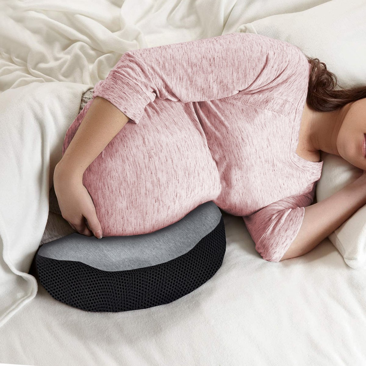 Eine schwangere Frau liegt mit einem Stützkissen auf dem Bett. Sie ruht und hält ihren Bauch.