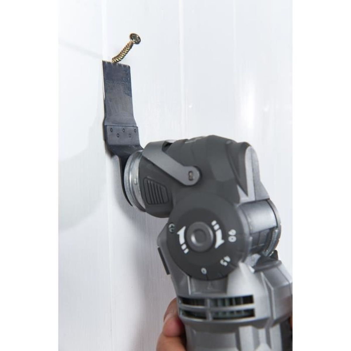 Oszillierendes Multi-Tool, das eine Schraube aus einer weißen Wand schneidet. Teil einer Hand ist zu sehen.