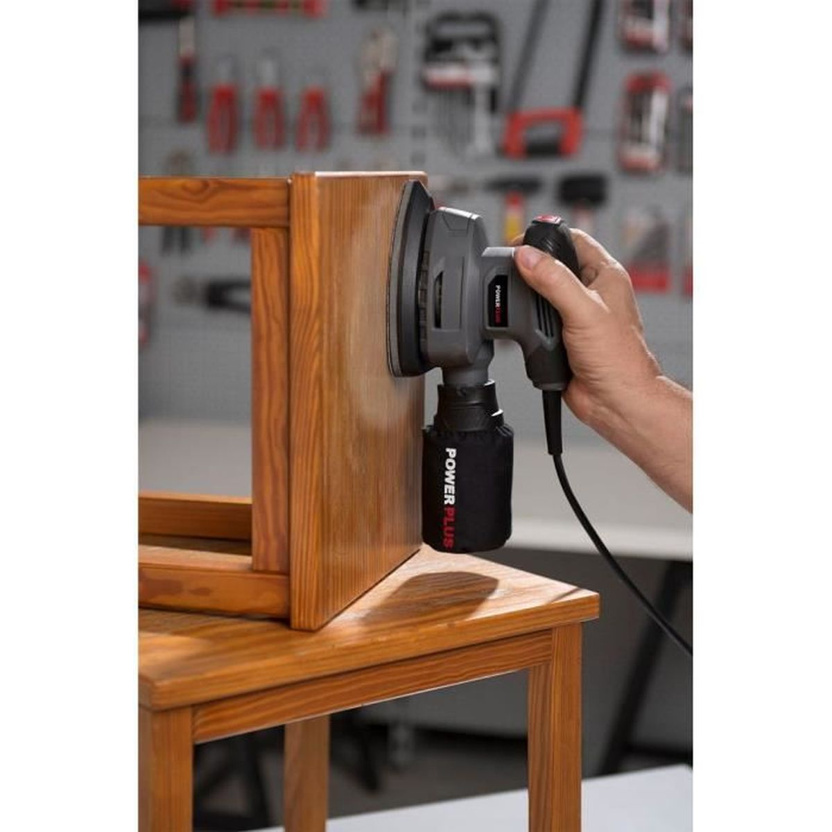 Eine Hand, die einen Elektroschleifer an einem Holzstuhlbein benutzt. Werkstatt Hintergrund.