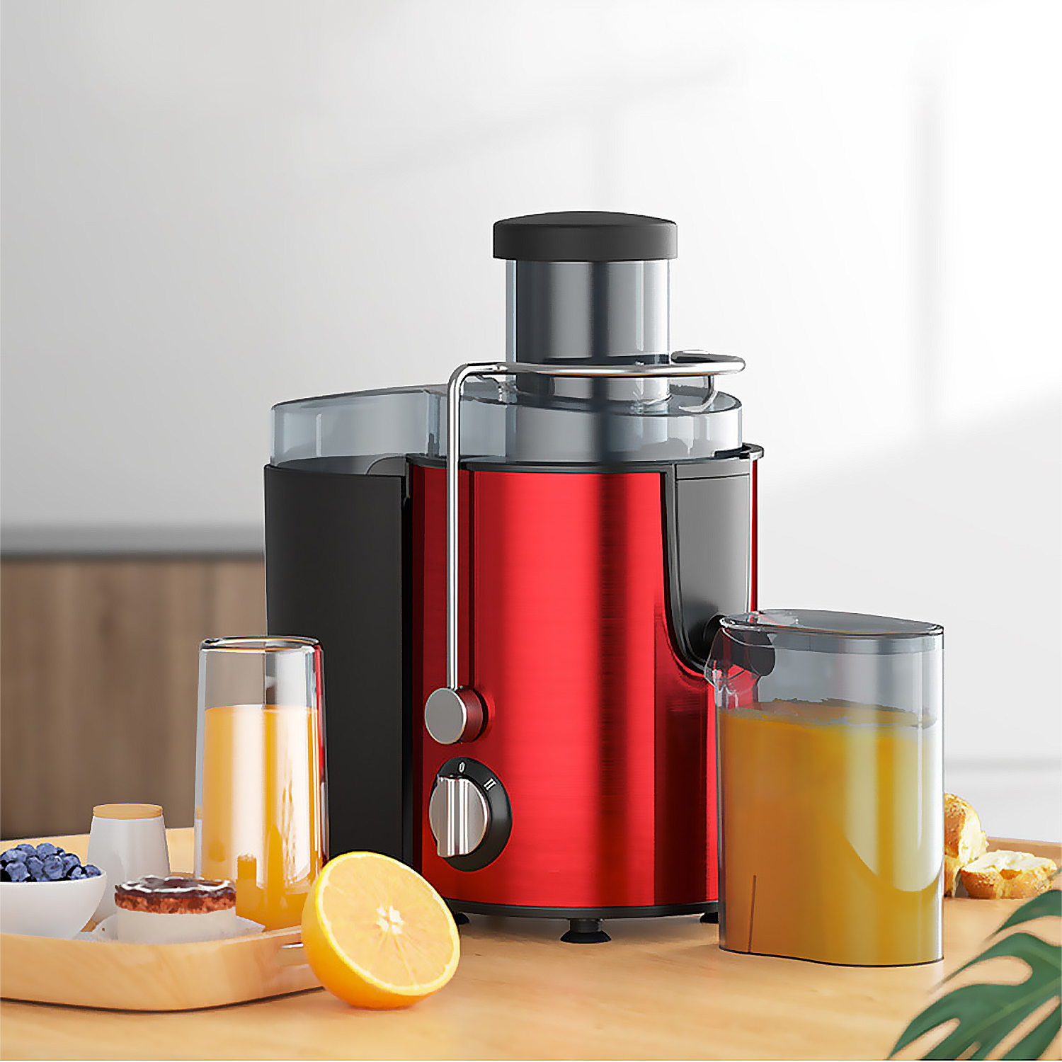 Exprimidor rojo con jugo en vasos y una bandeja con fruta. Se ve media naranja y un pastel.