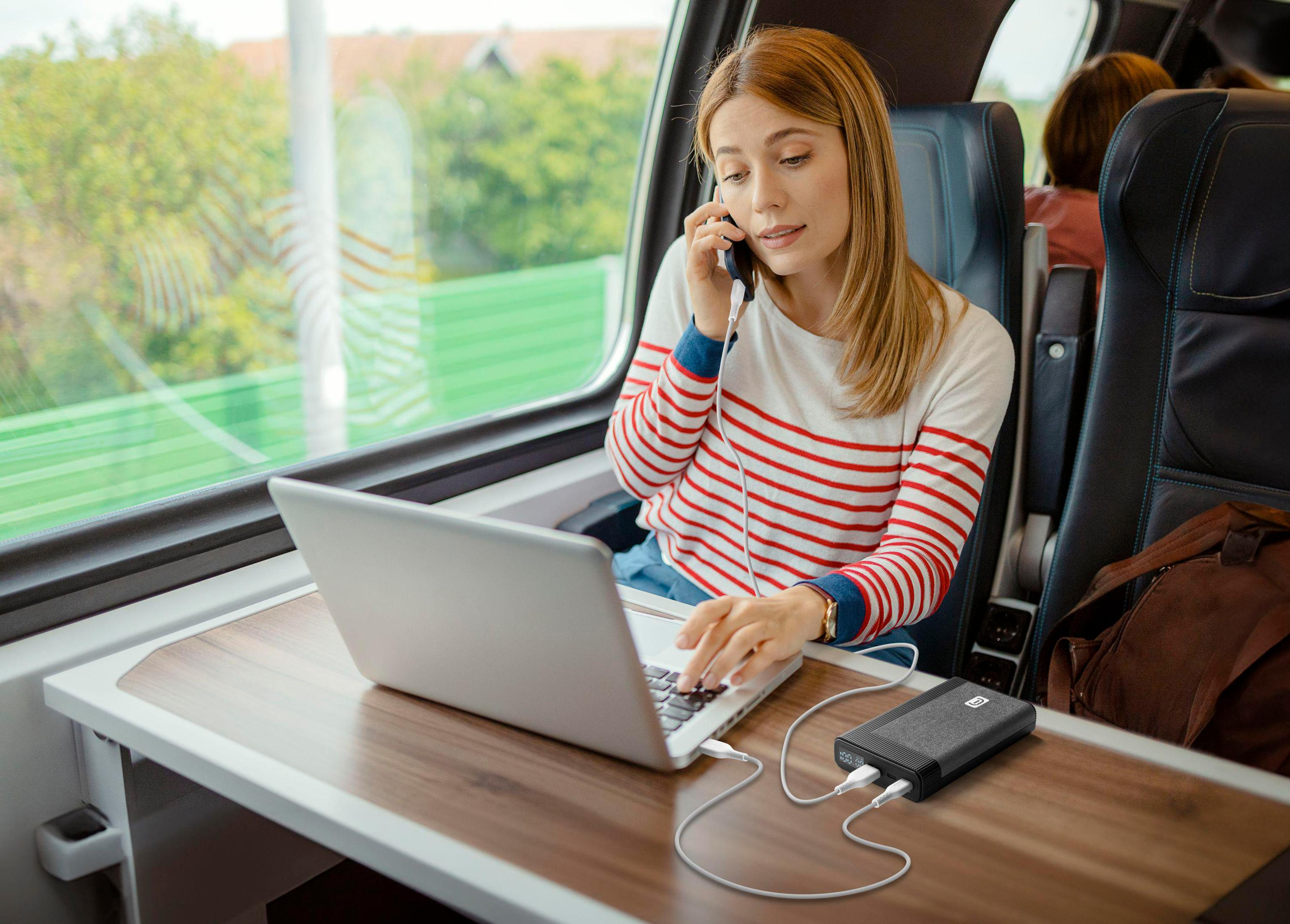 Una donna che usa un laptop e parla al telefono in un treno, con un power bank.