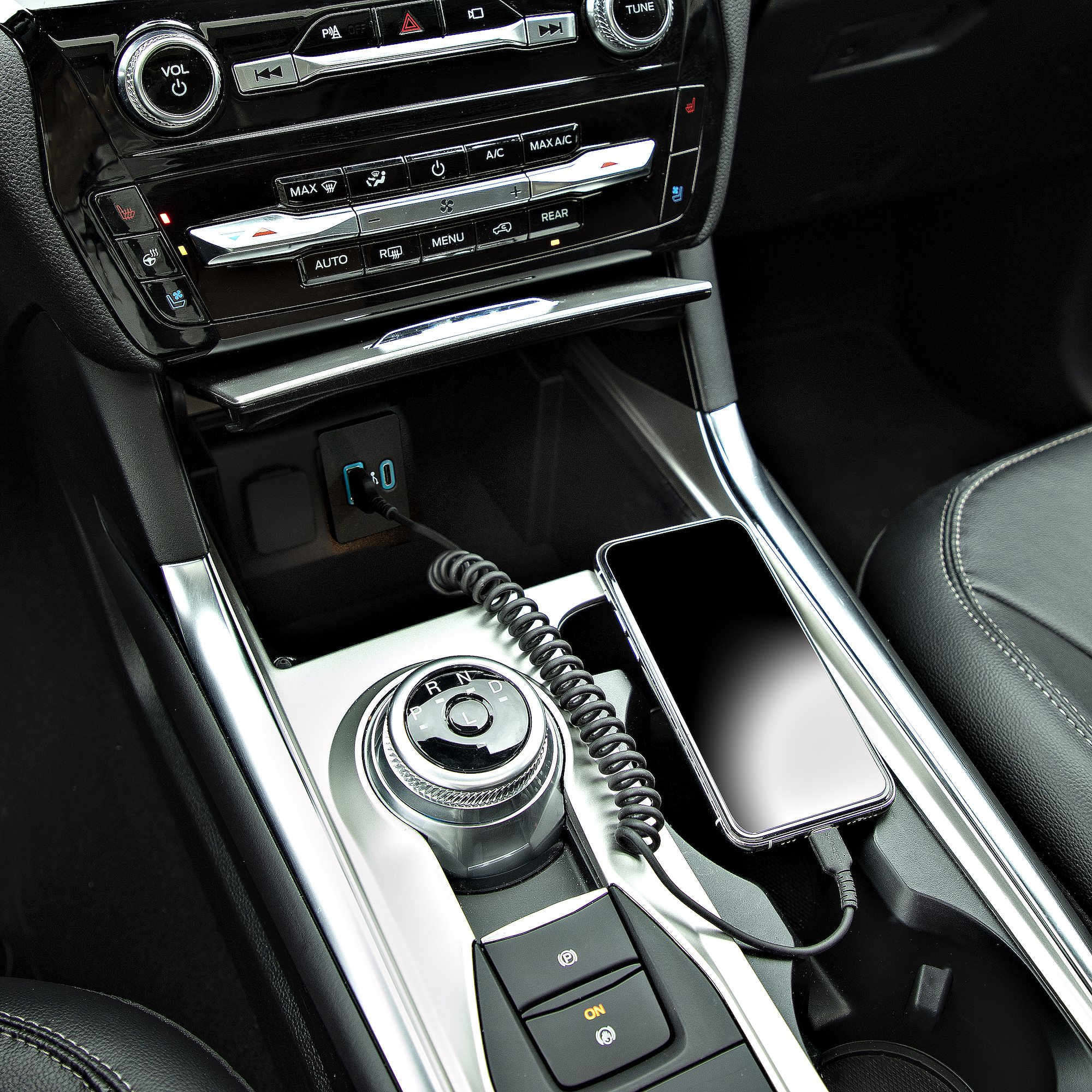 Interno auto con telefono collegato a un cavo di ricarica nella console centrale.