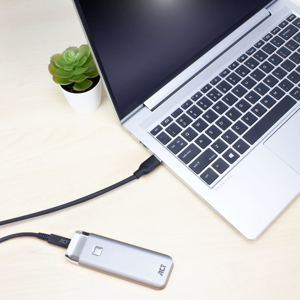 Een laptop aangesloten op een zilveren externe harde schijf, beide op een houten bureau, met een plant.