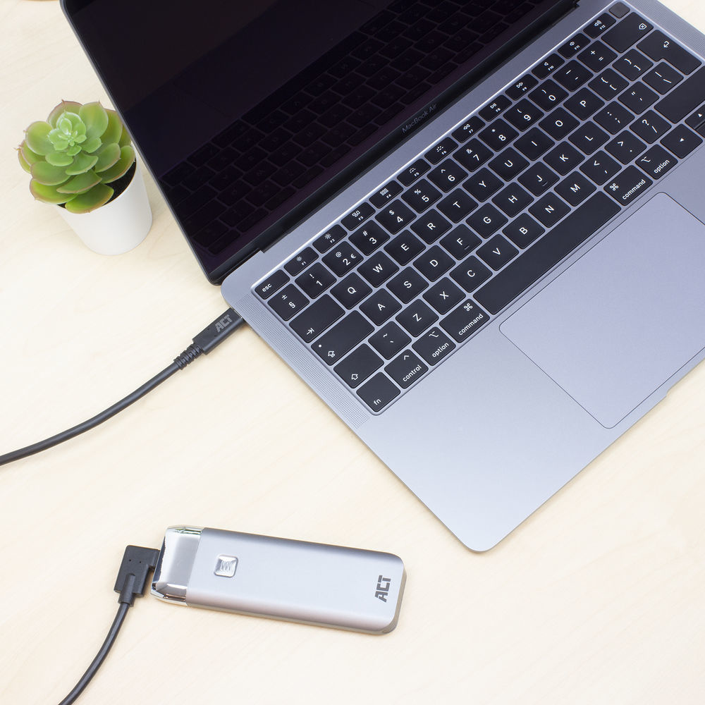 Laptop verbonden met een zilverkleurig apparaat via een USB-kabel, op een houten tafel, met een plant.