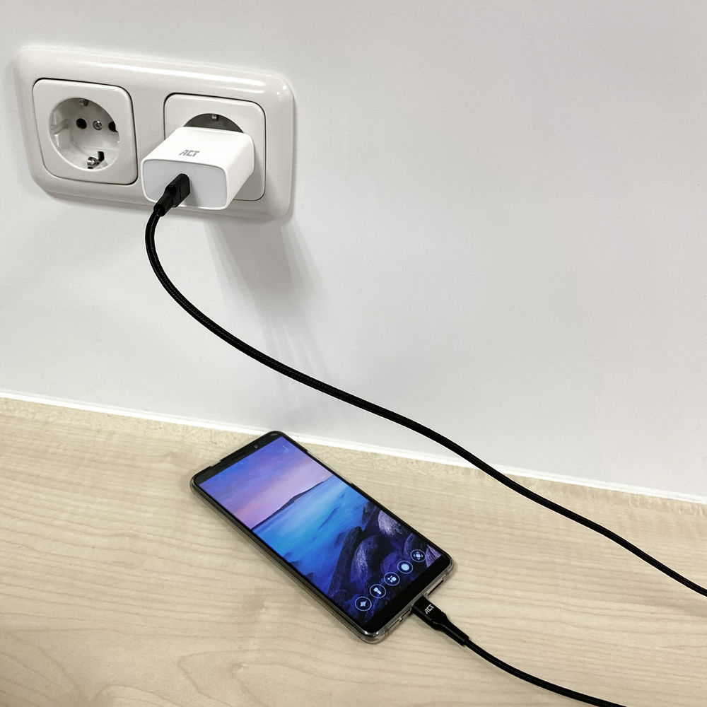 Un téléphone est branché sur un chargeur mural. Le téléphone et le chargeur sont blancs. Le fond est un mur.