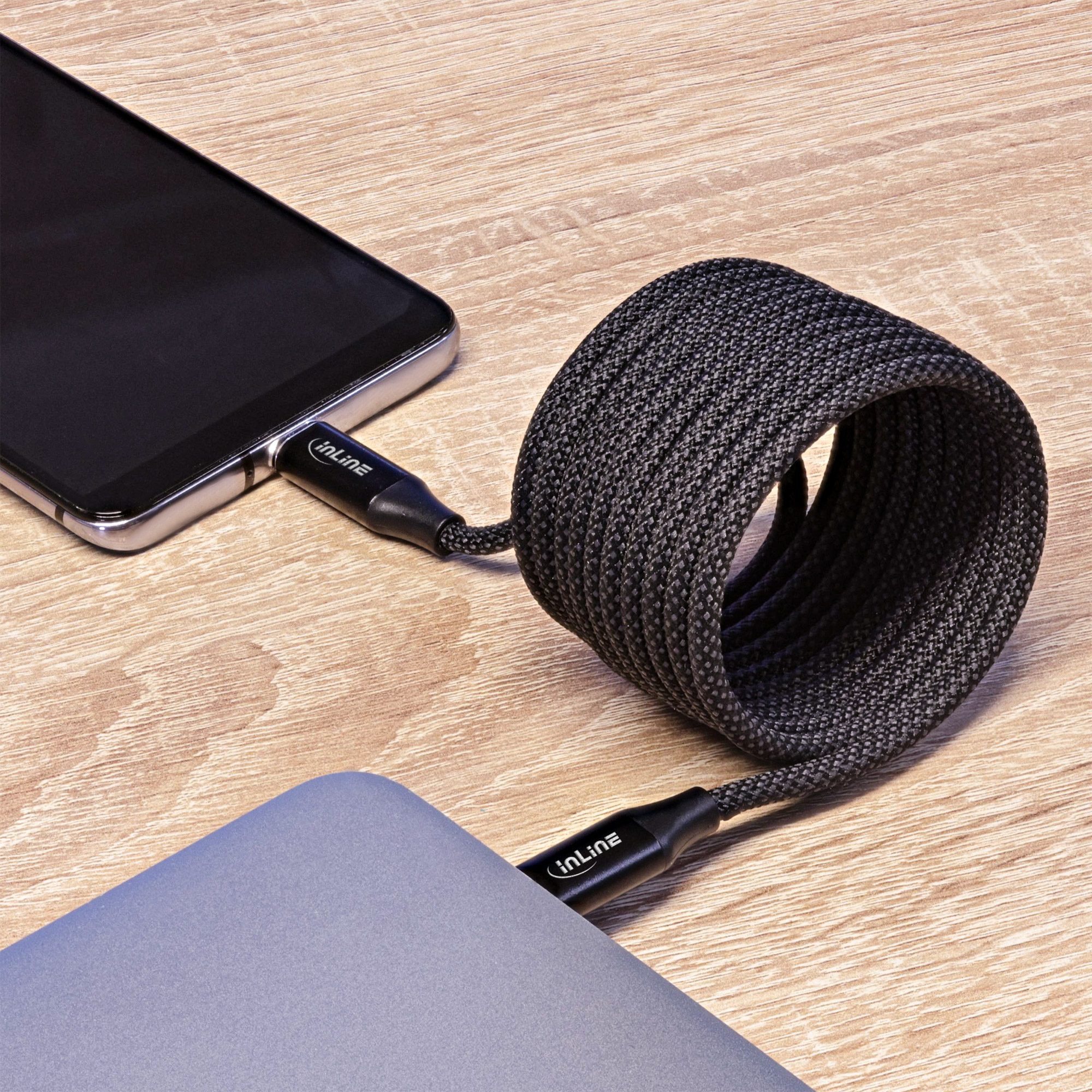 Câble USB-C noir connecté à un téléphone et un ordinateur portable. Le câble est tressé et enroulé.