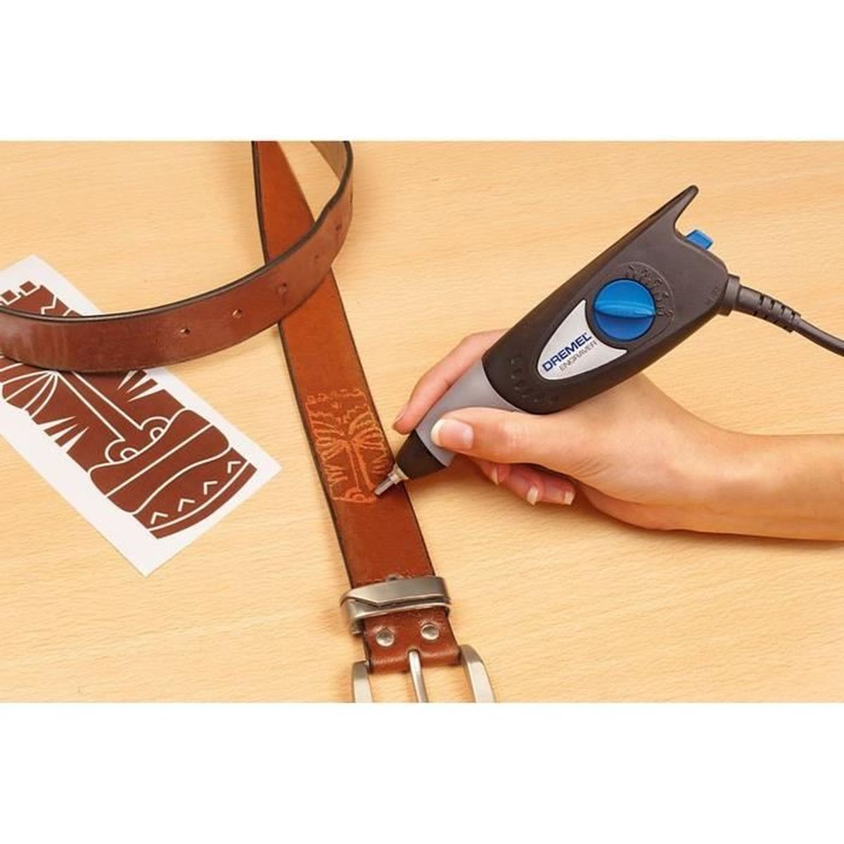 Ręka graweruje skórzany pasek za pomocą Dremela. Widoczny jest również szablon i klamra.