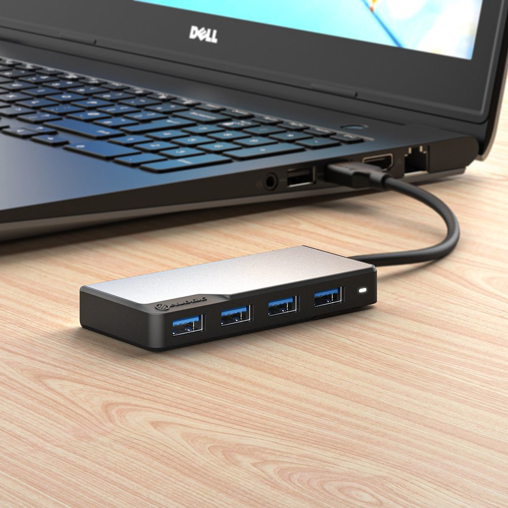 Laptop nero collegato a un hub USB nero con quattro porte USB su un tavolo di legno.