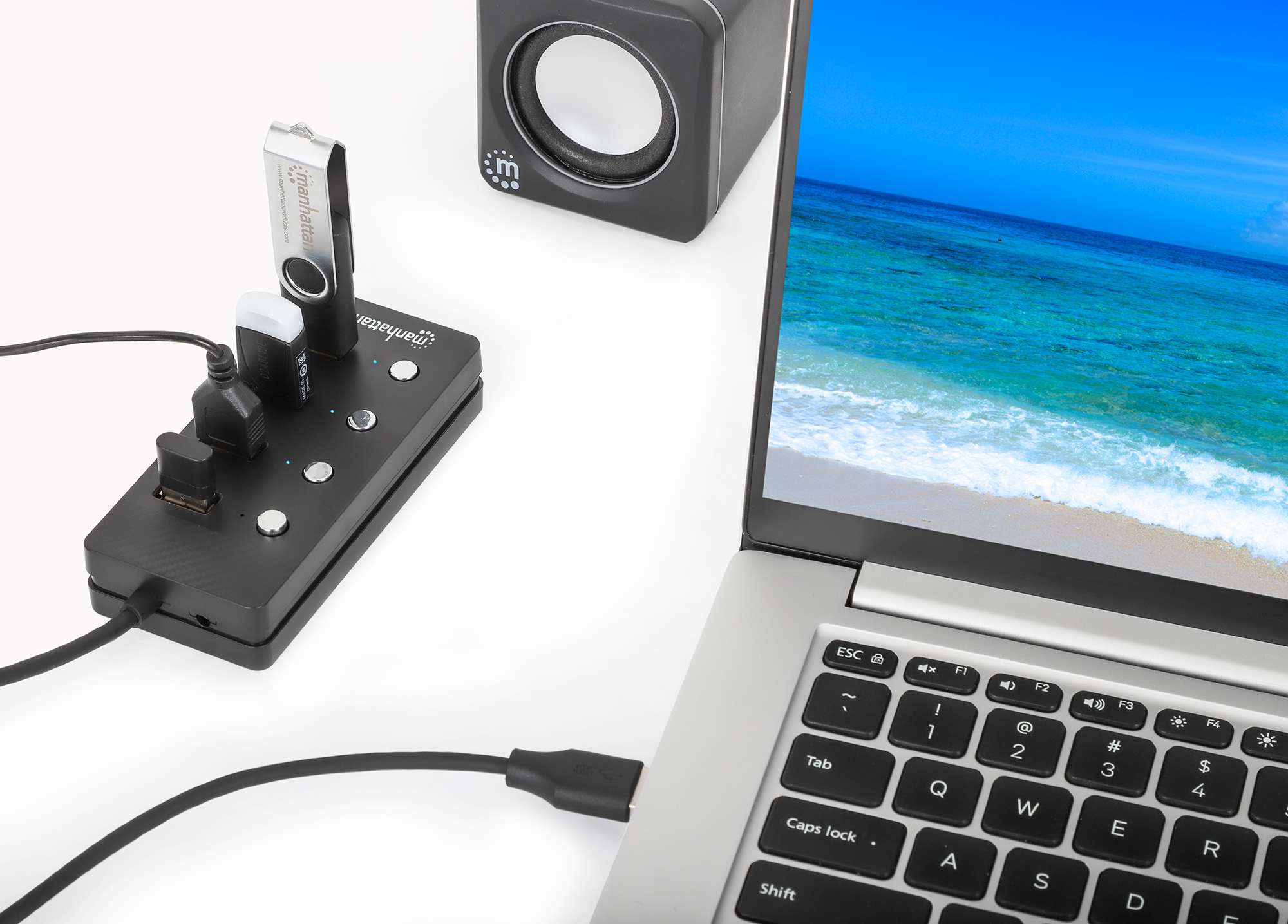 Laptop con hub USB, altoparlante e scena di spiaggia sullo schermo. Diversi dispositivi USB collegati.