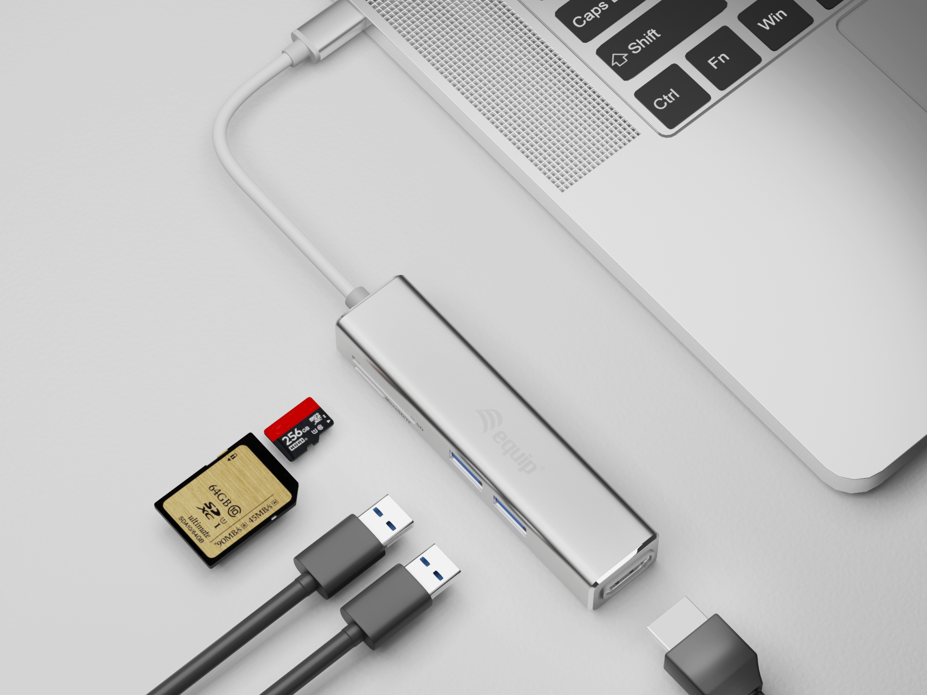 Un hub USB argentato collegato a un laptop. Una scheda SD e due cavi USB sono vicini.