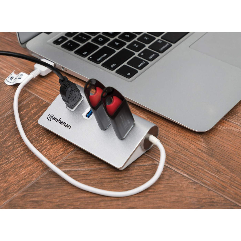 Laptop con un hub USB argento e due unità USB rosse collegate, su un tavolo di legno.