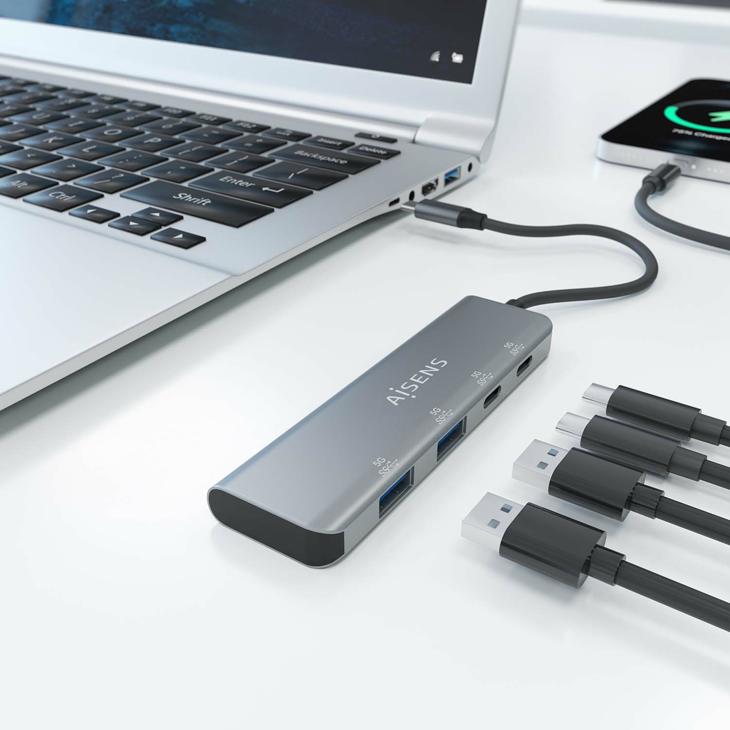 Laptop con un hub USB grigio collegato e tre cavi USB, e un telefono in carica.