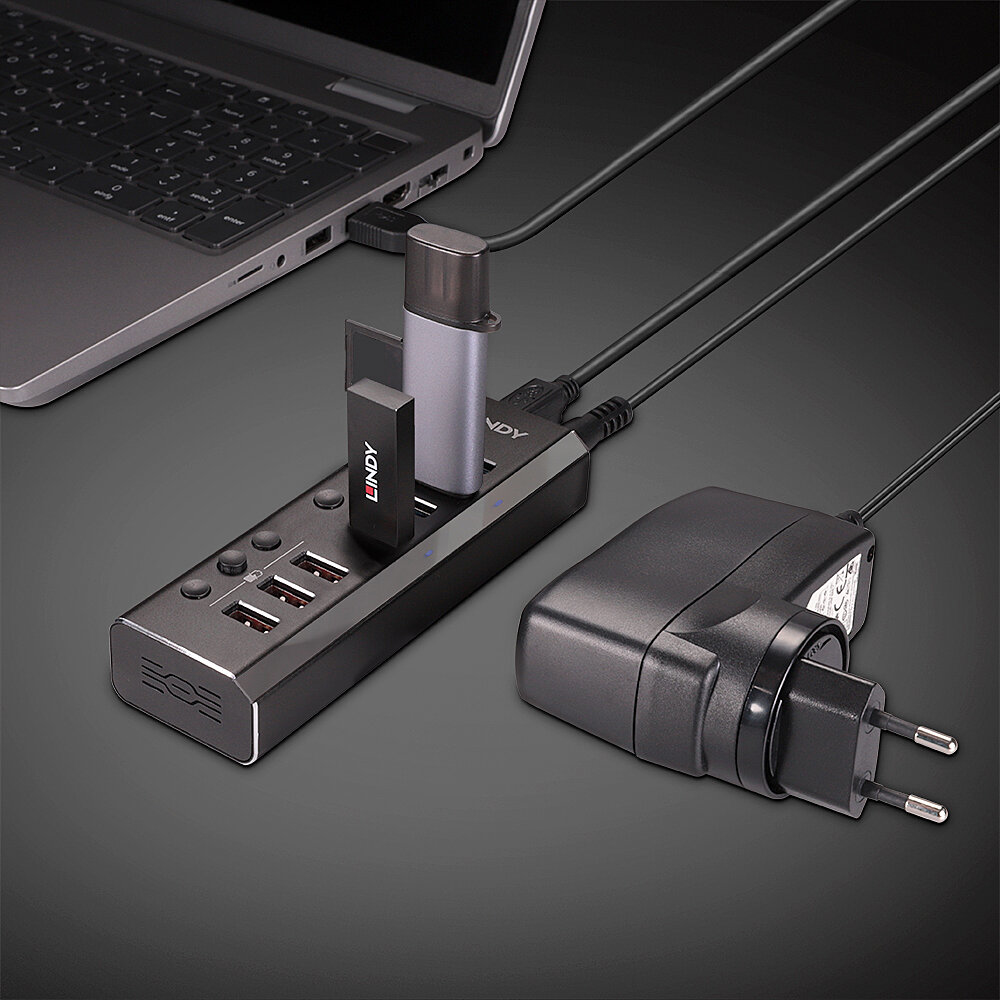 Laptop, hub USB con chiavette USB e alimentatore su superficie scura.