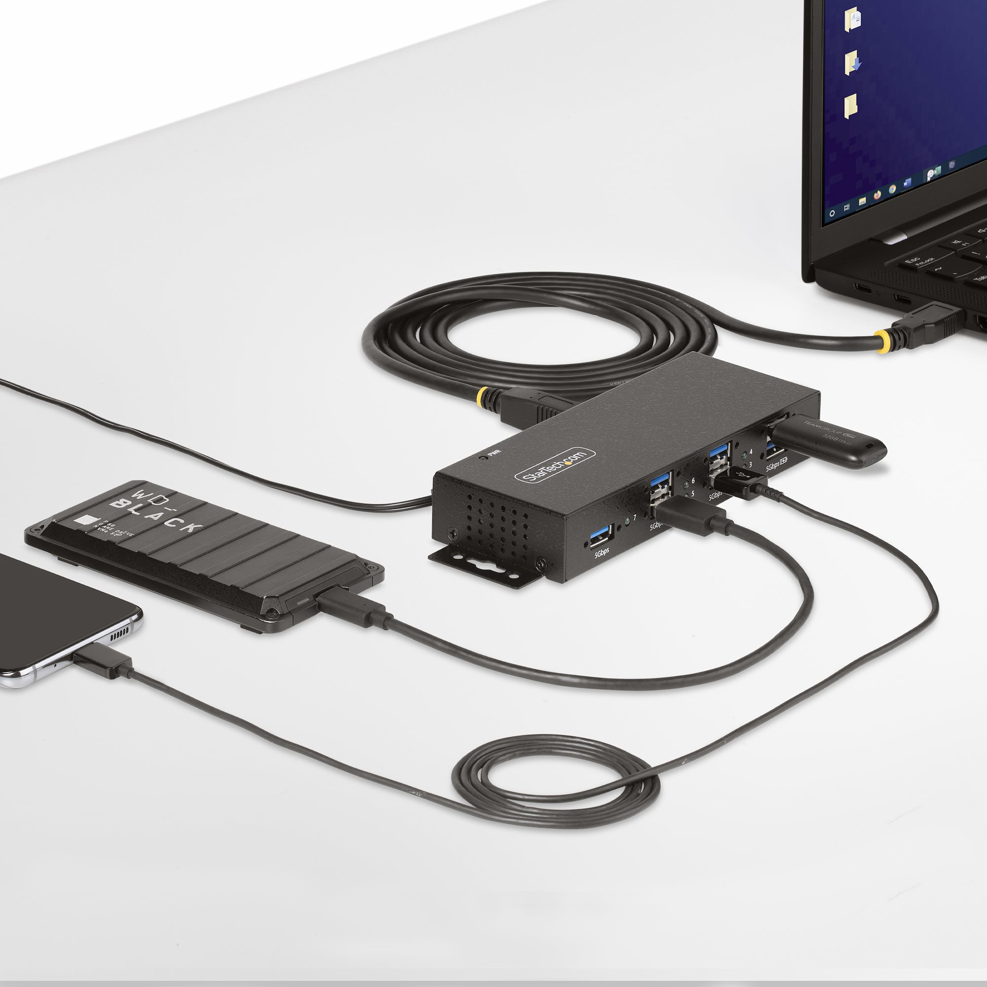 Configurazione da scrivania con laptop, hub, hard disk esterno e telefono collegati. Cavi visibili.