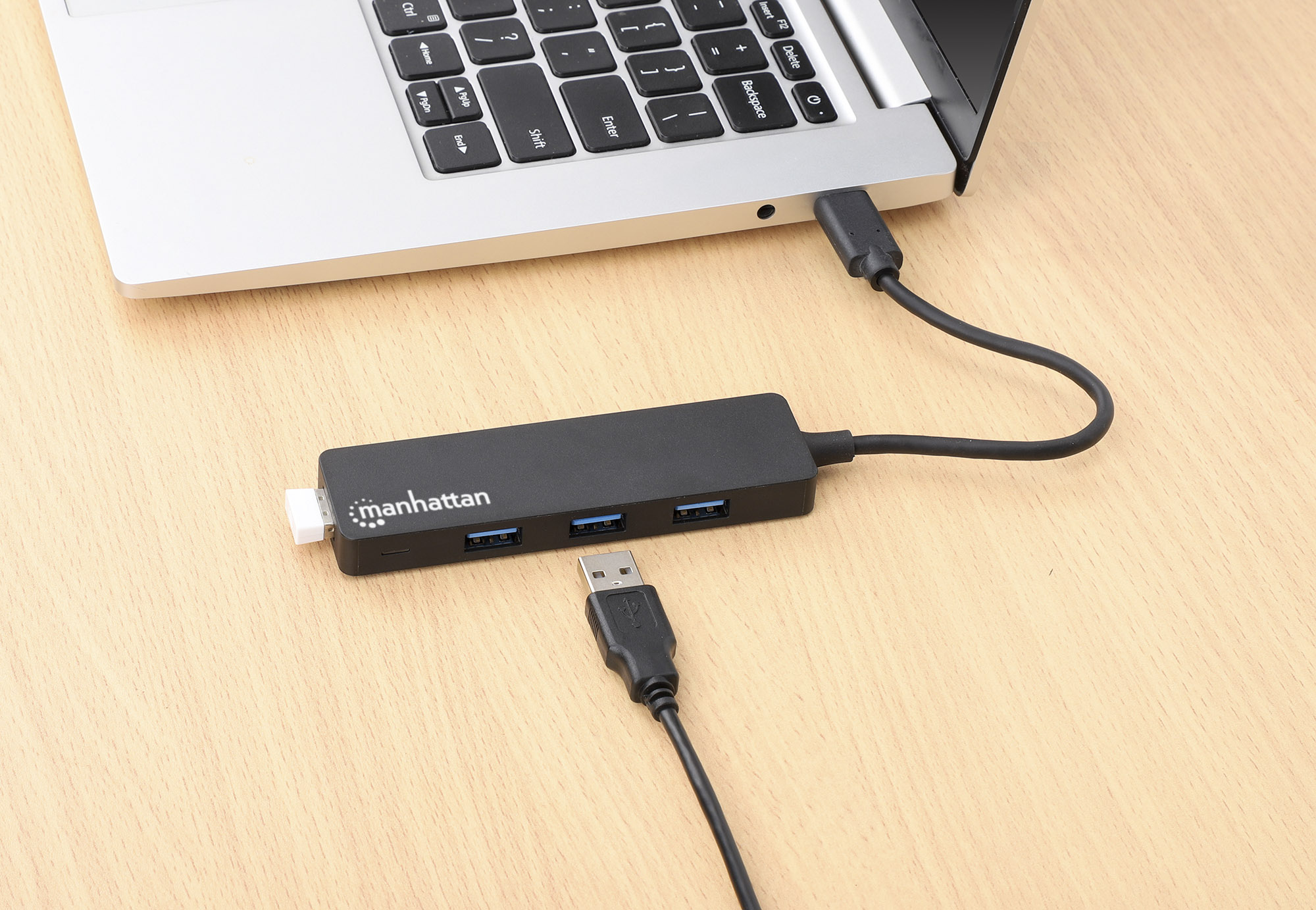 Hub USB nero collegato a un laptop su una scrivania di legno. Un altro cavo USB è visibile.