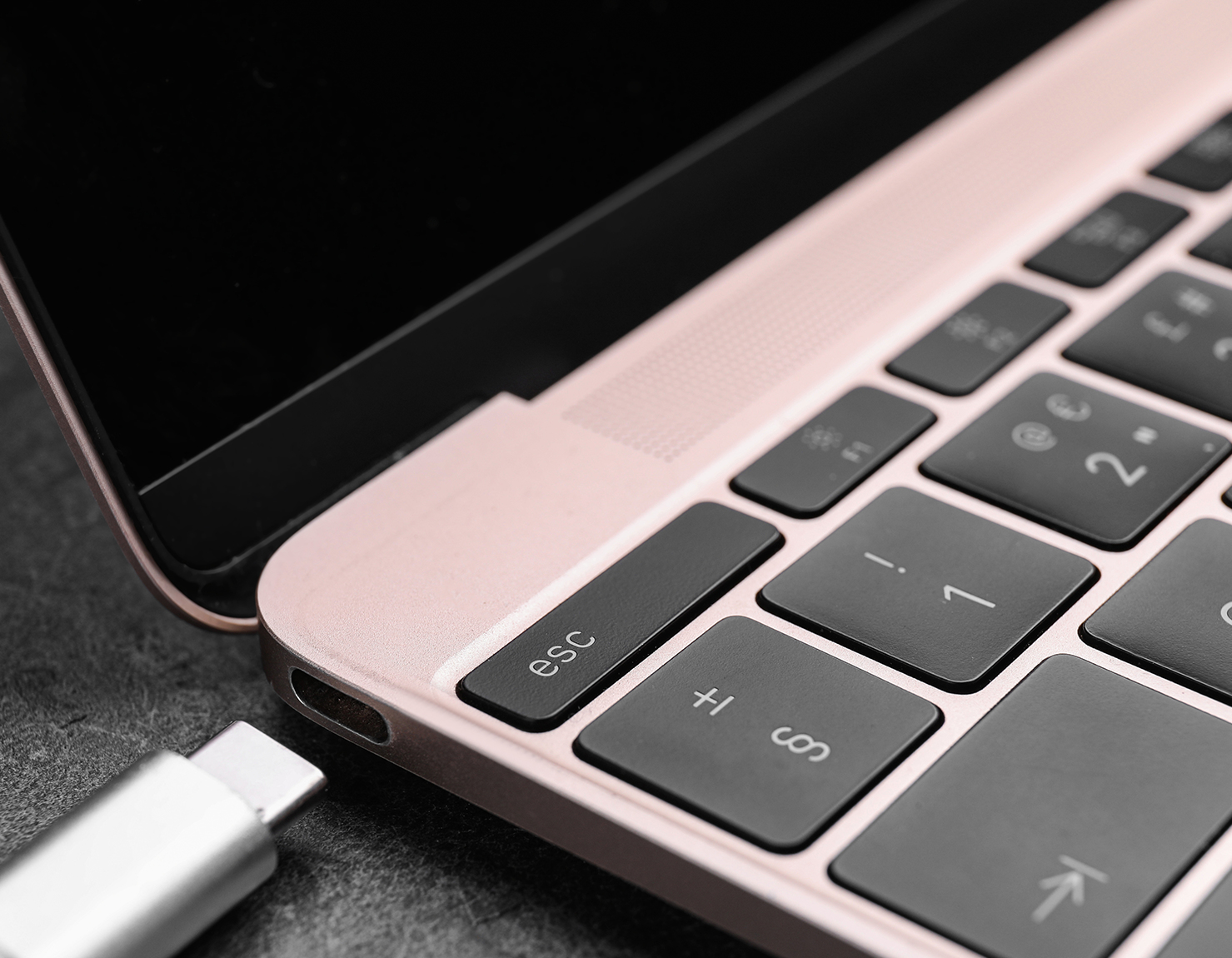 Primo piano di una tastiera di un laptop e della sua porta USB-C con un cavo argentato collegato.