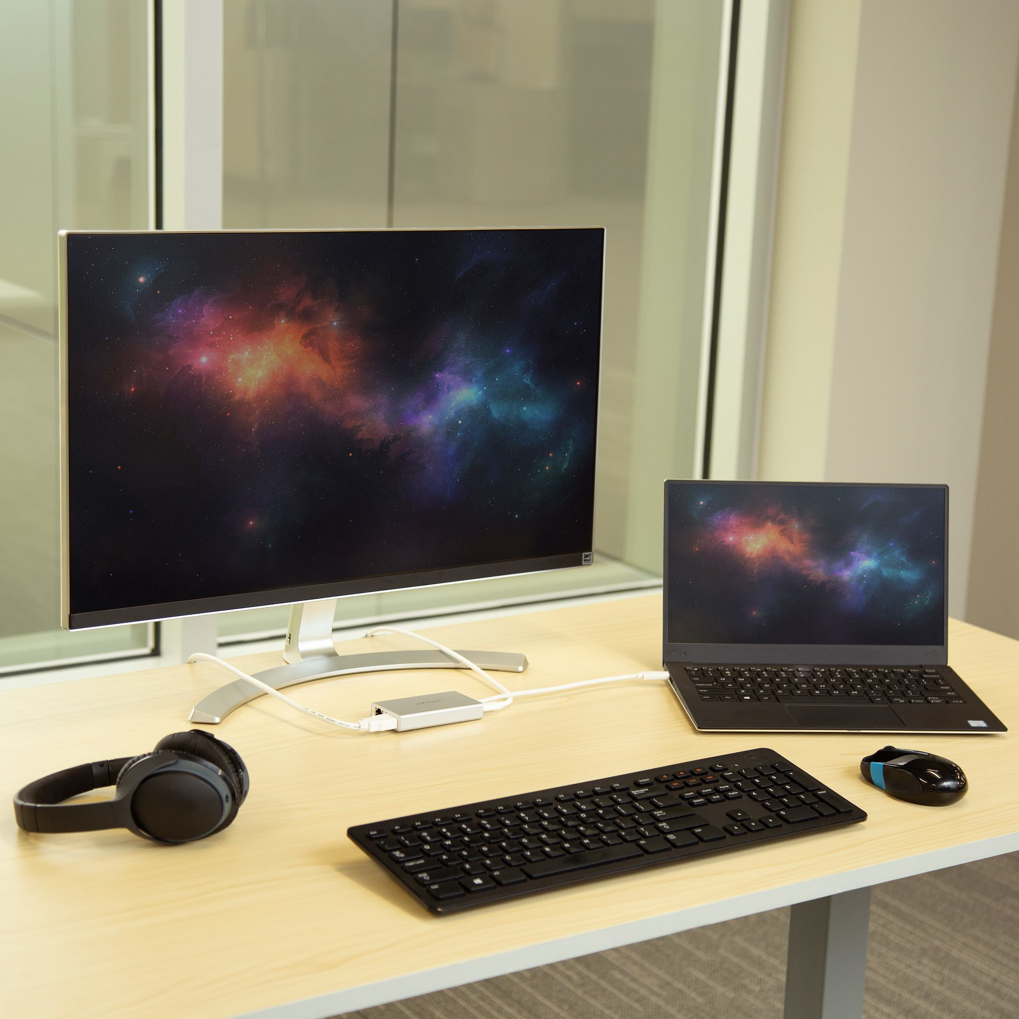 Una scrivania con monitor, laptop, tastiera, mouse e cuffie. Un hub li collega.