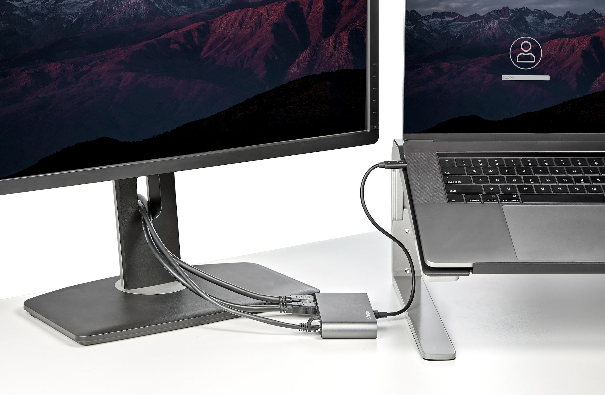 Un laptop collegato a un monitor e a un hub. Scrivania bianca e sfondo nero.