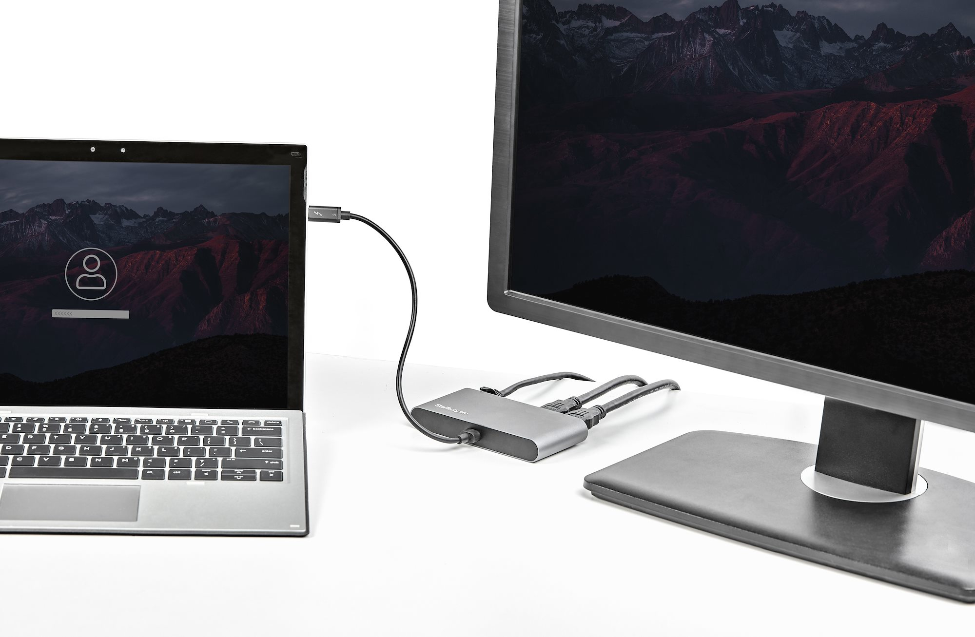 Laptop collegato a un monitor e un hub USB su una scrivania bianca, in un ambiente.