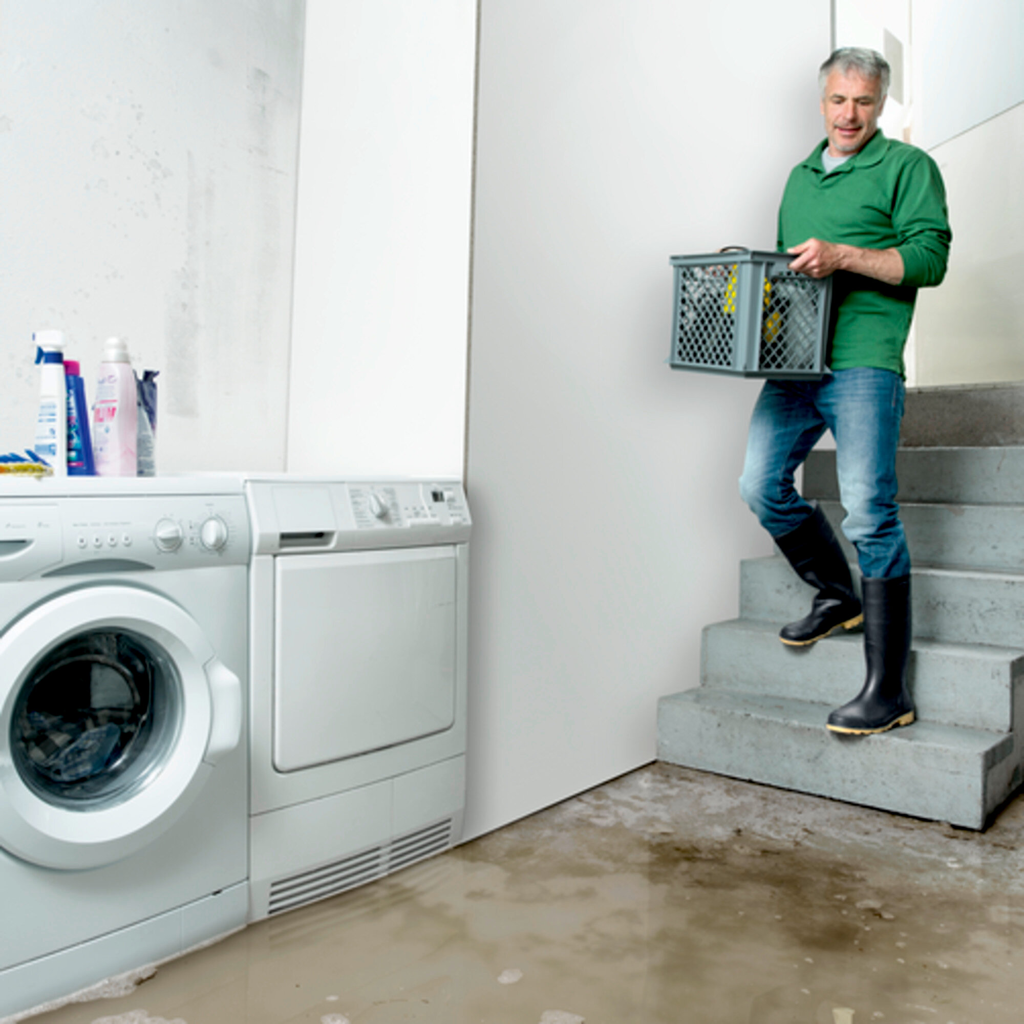 Ein Mann in grünem Hemd und Jeans trägt eine Kiste die Treppe hoch. Der Boden ist überflutet.