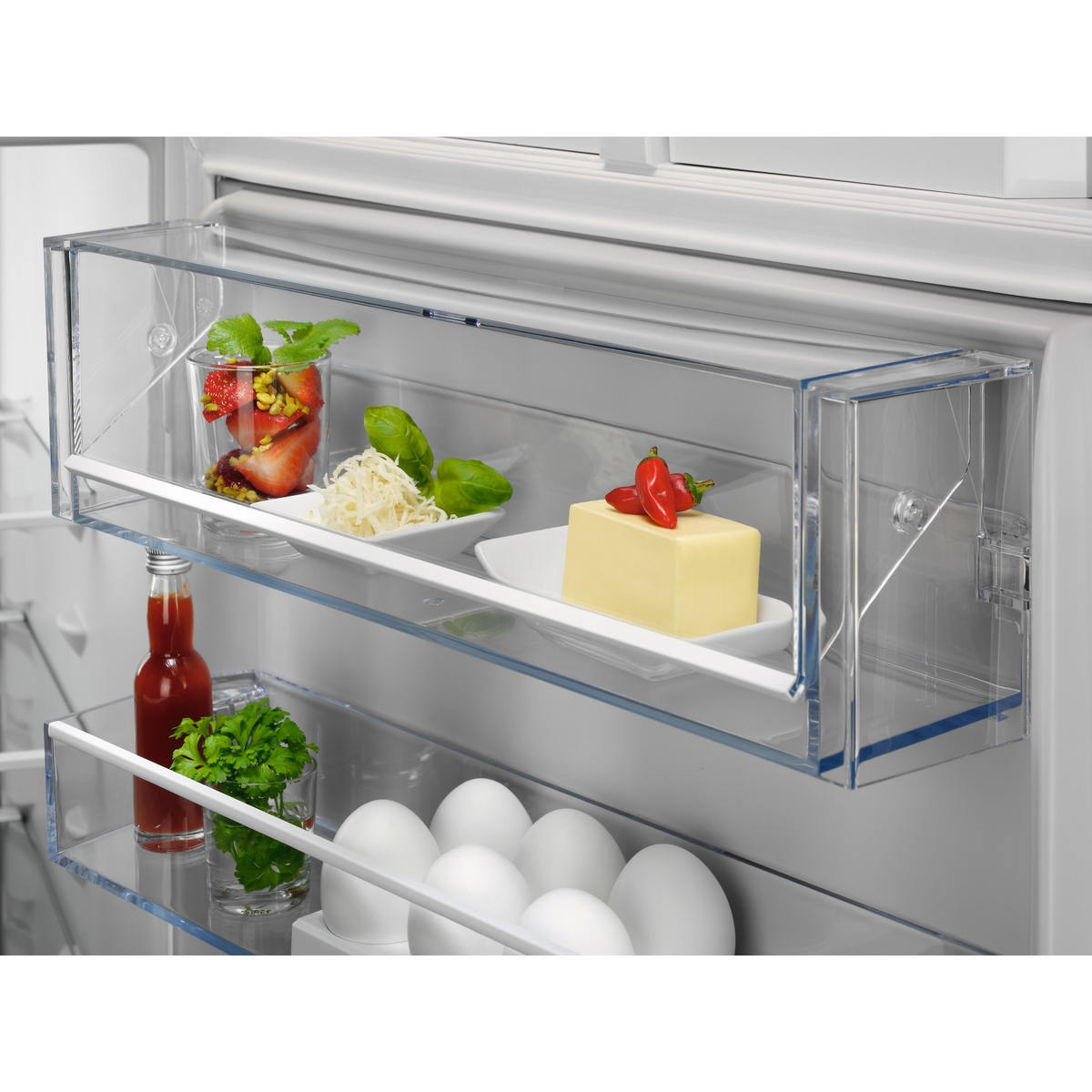 Interior de nevera con estantes de vidrio. Contiene alimentos como frutas, queso, mantequilla y huevos.