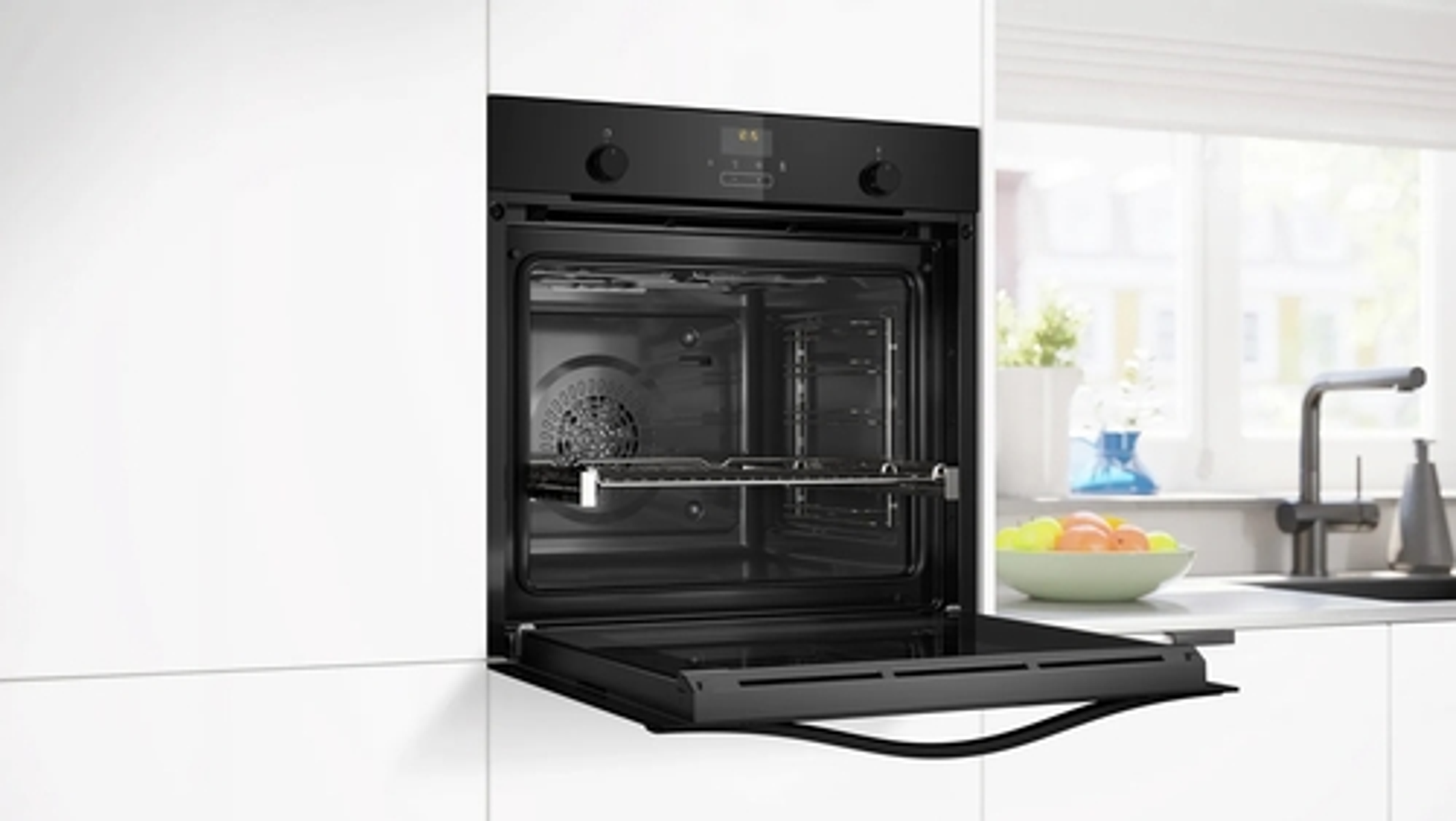 Horno empotrado negro con la puerta abierta, dentro de una cocina blanca.