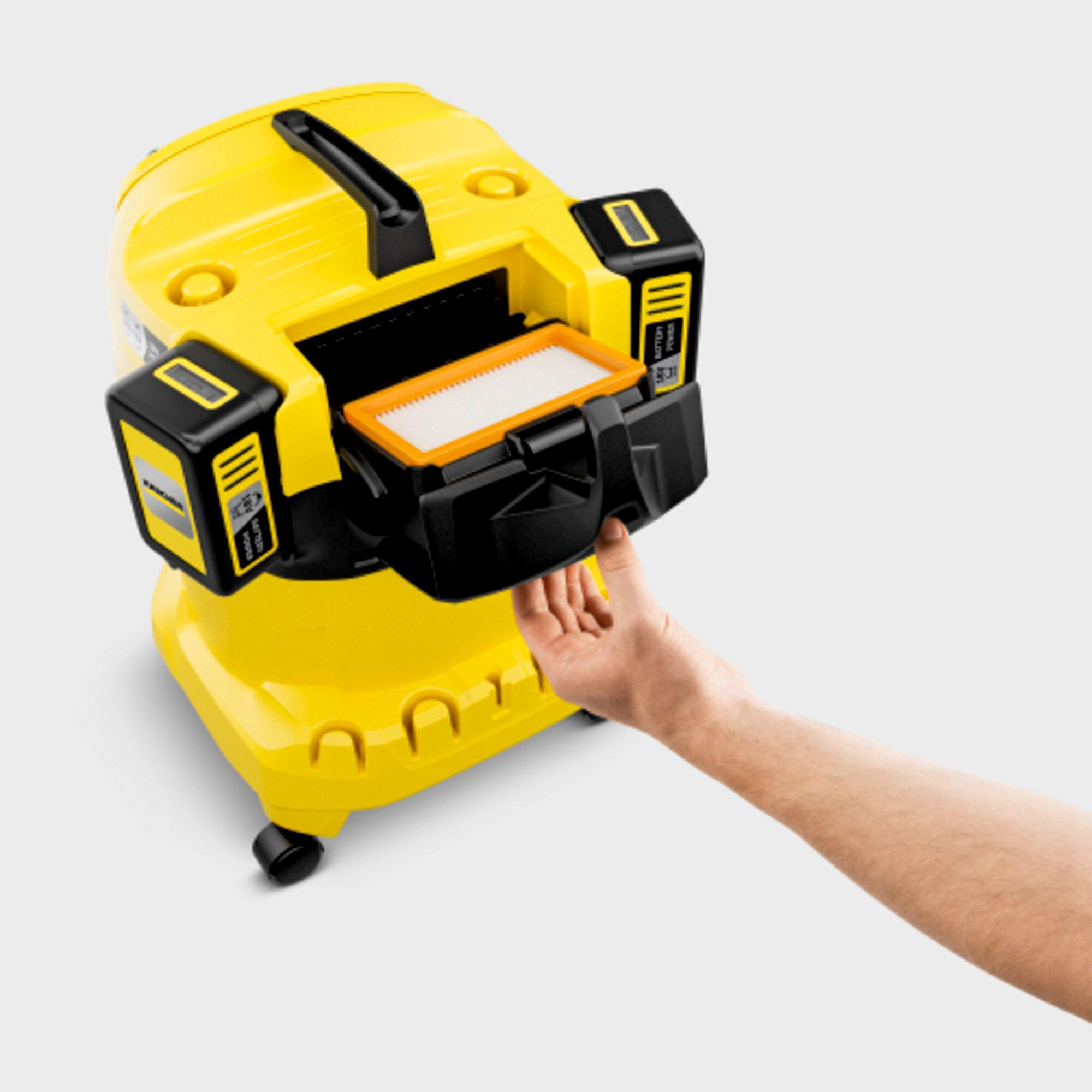 Un aspirapolvere giallo con la mano di una persona che raggiunge un filtro.