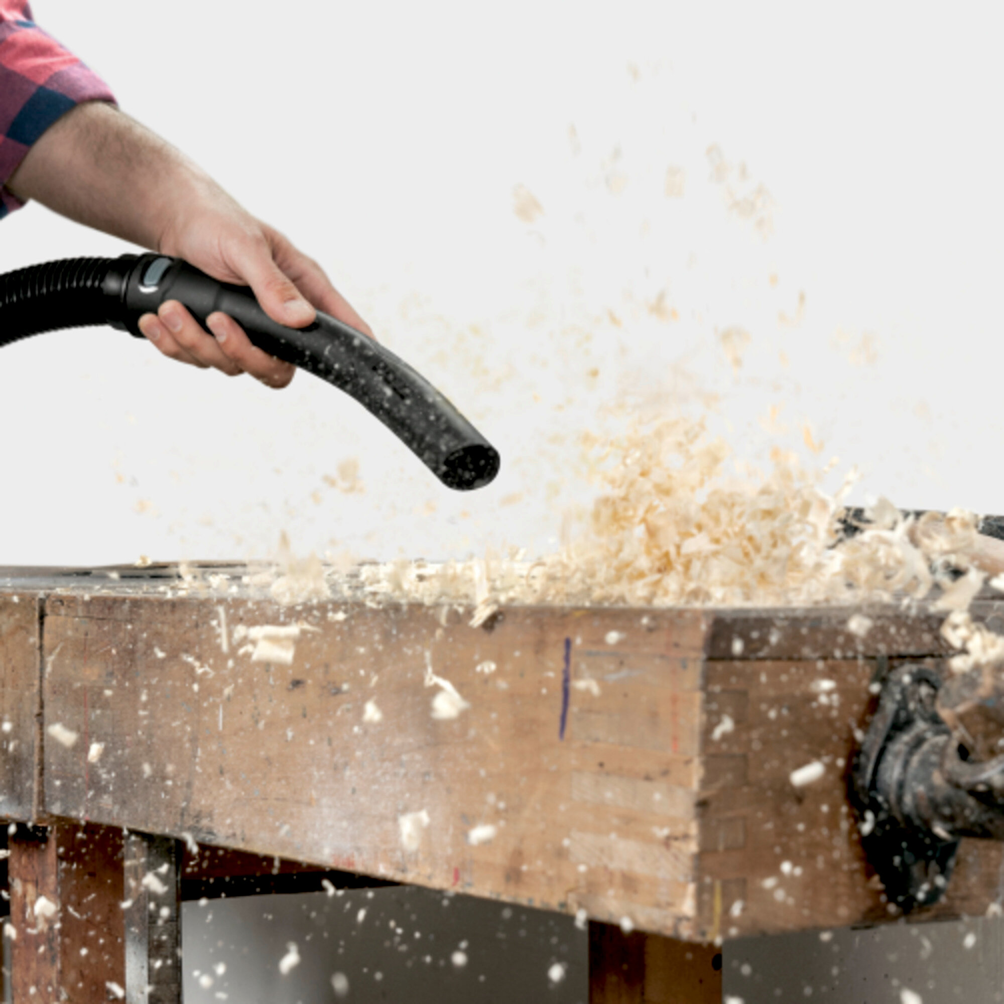 Eine Hand benutzt einen Staubsauger, um Holzspäne von einer Werkbank aufzusaugen.