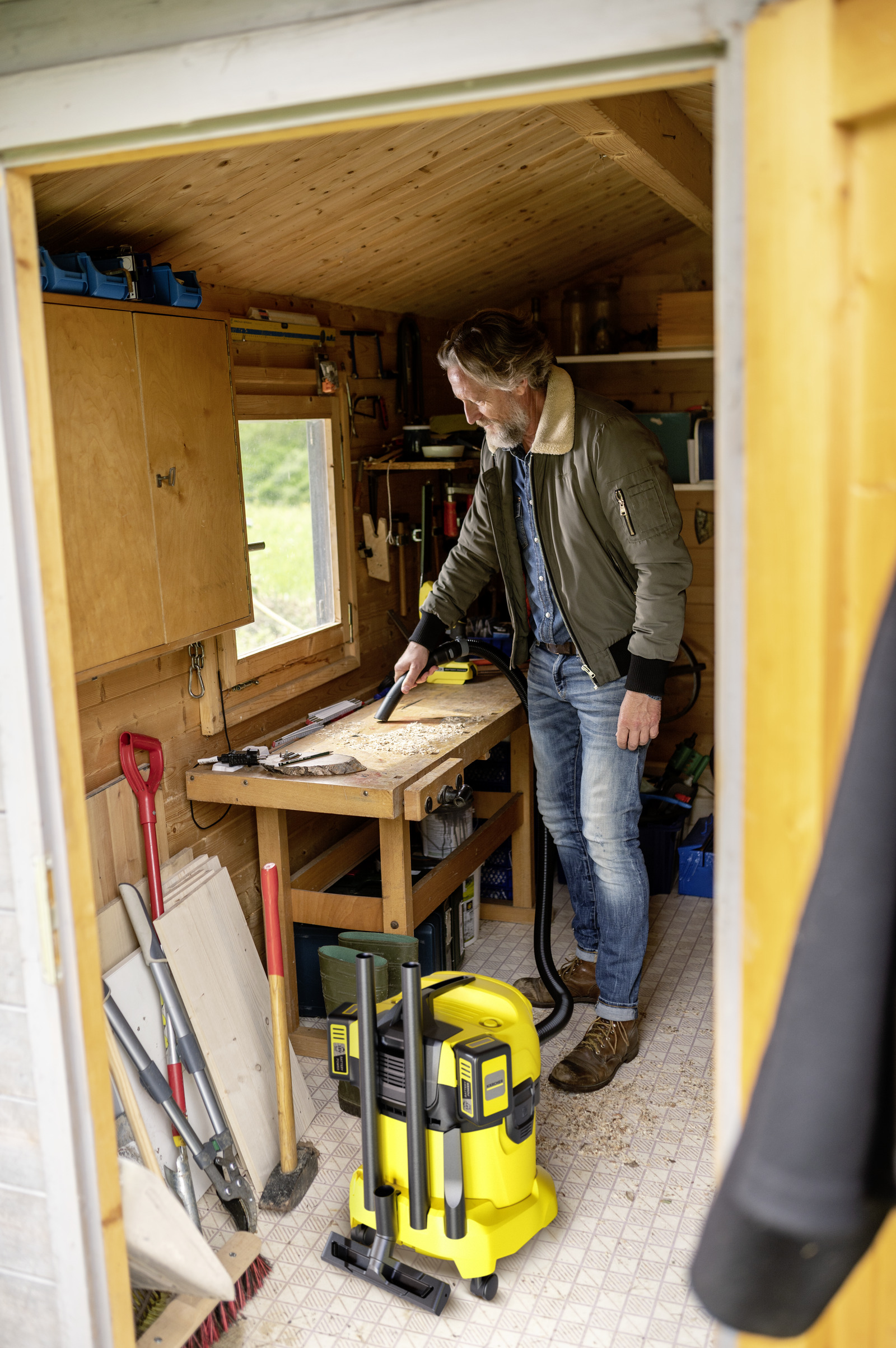 Mann in einem Schuppen arbeitet an einer Werkbank mit Werkzeugen und einem gelben Staubsauger.