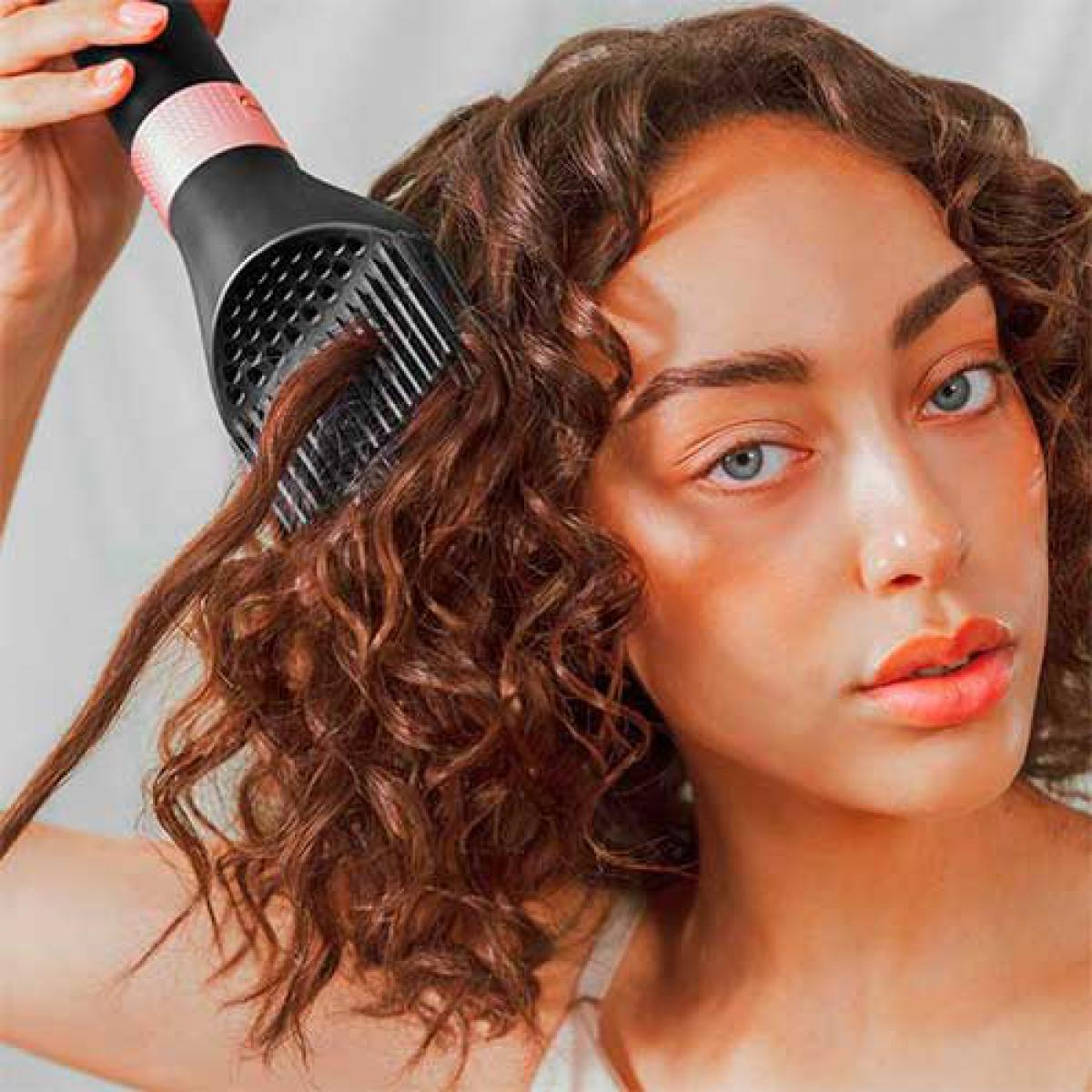 Mujer secando cabello rizado con secador negro y rosa. Fondo blanco.