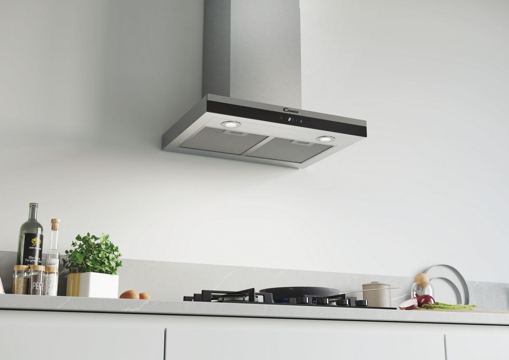 Una campana extractora está instalada. Es plateada y negra. Una estufa y algunos elementos están en primer plano.