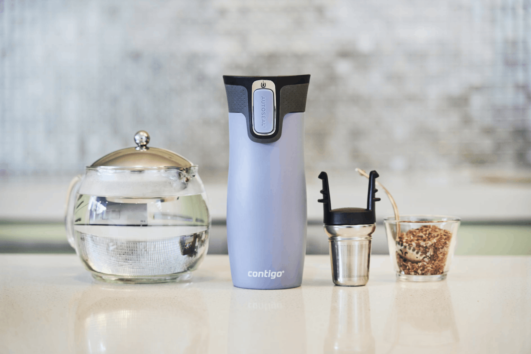 Un termo Contigo, una tetera de vidrio, un infusor de té y un frasco de vidrio con hojas de té.