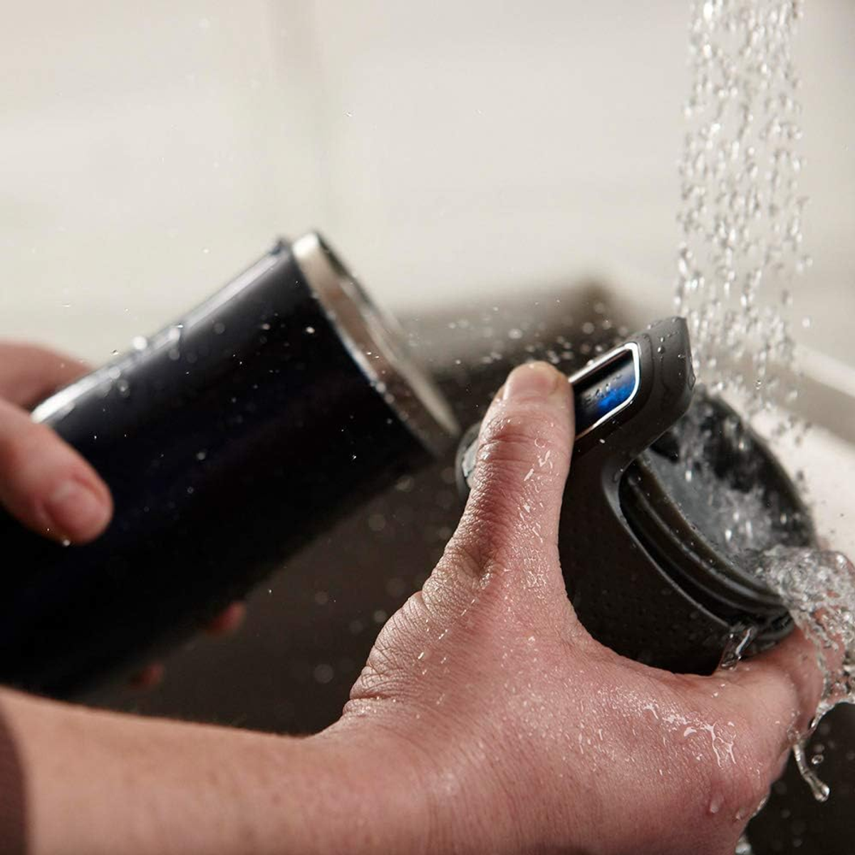 Manos lavando un objeto negro bajo agua corriente. Agua salpicando.