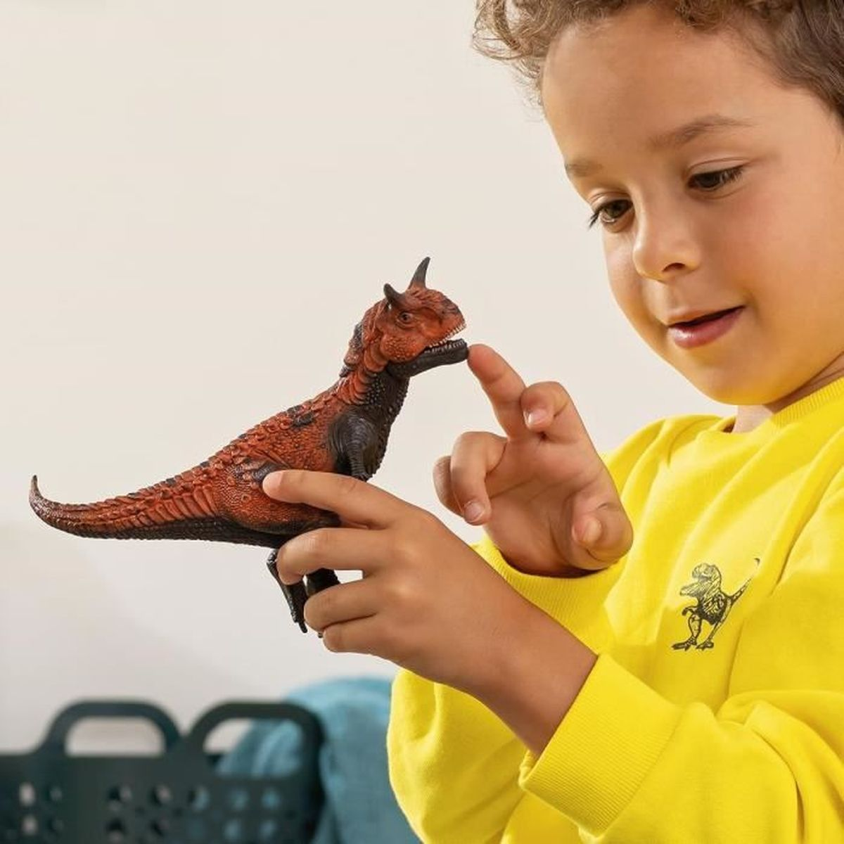 Een kind raakt een speelgoeddinosaurus aan. De dinosaurus is bruin en heeft rode details. Het kind lacht.