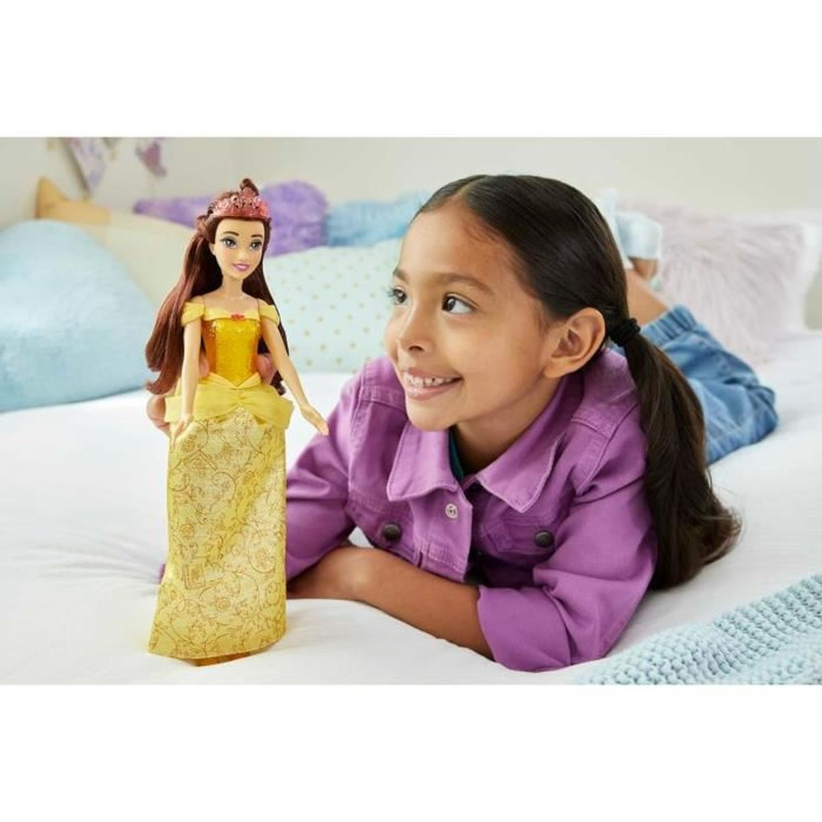 Ein junges Mädchen lächelt eine Puppe von Belle an. Die Puppe trägt ein gelbes Kleid und eine Tiara.