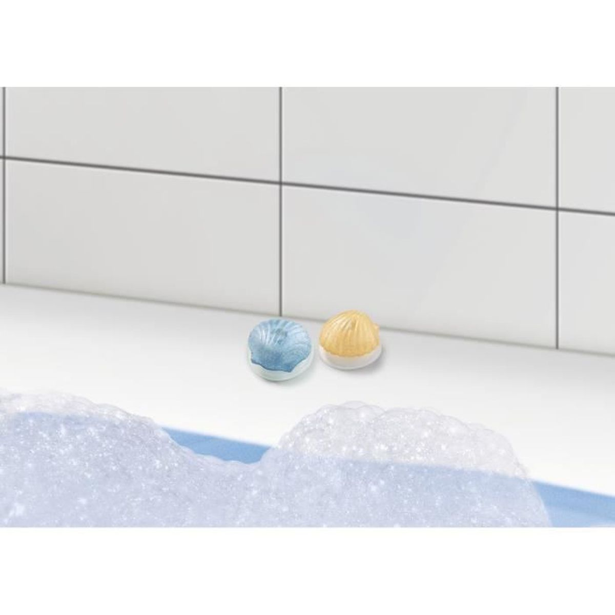 Zwei Badebomben, eine blaue und eine gelbe, auf einer weißen Oberfläche mit Schaum. Weißer gefliester Hintergrund.