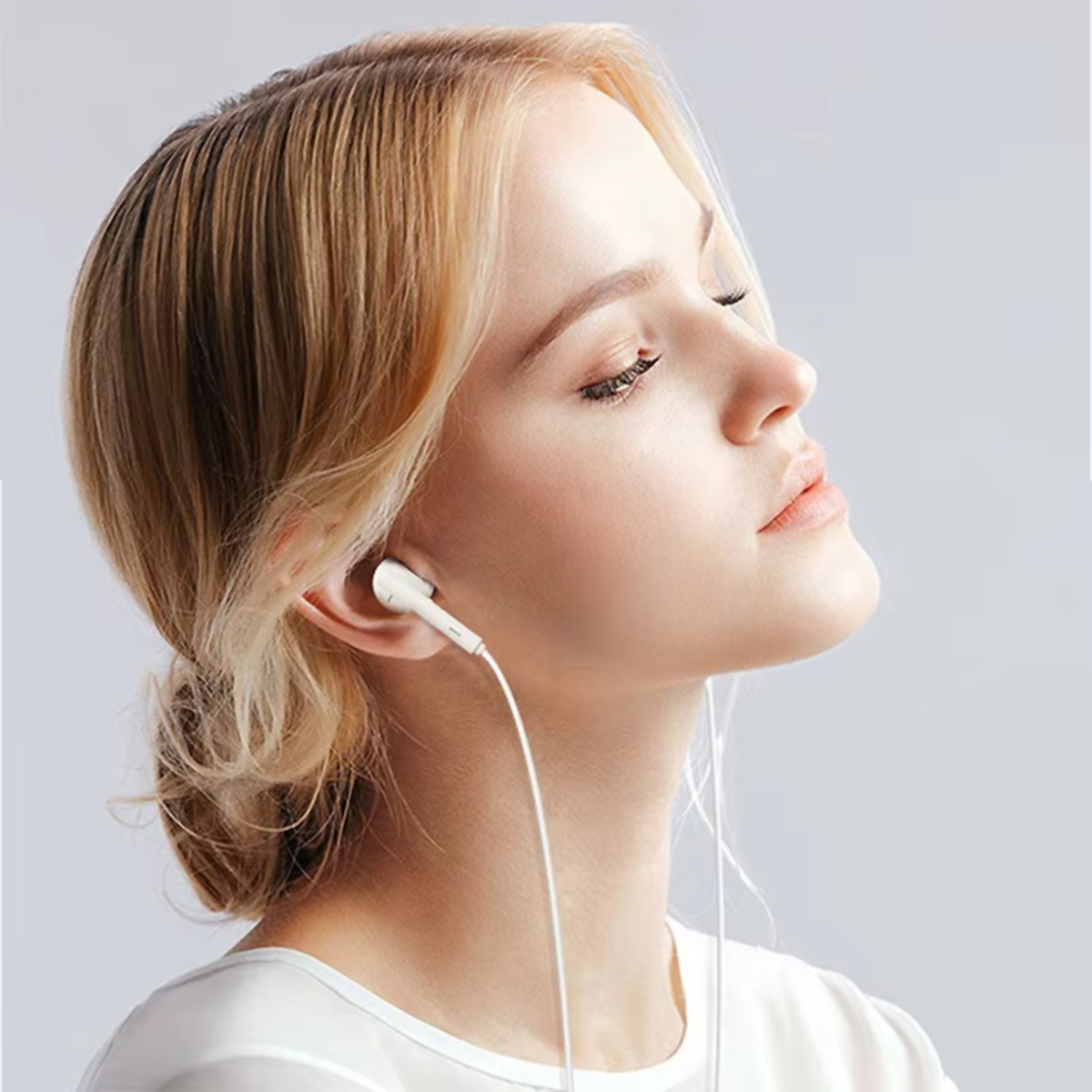 Una mujer con auriculares, ojos cerrados, mirando hacia arriba, con fondo claro.