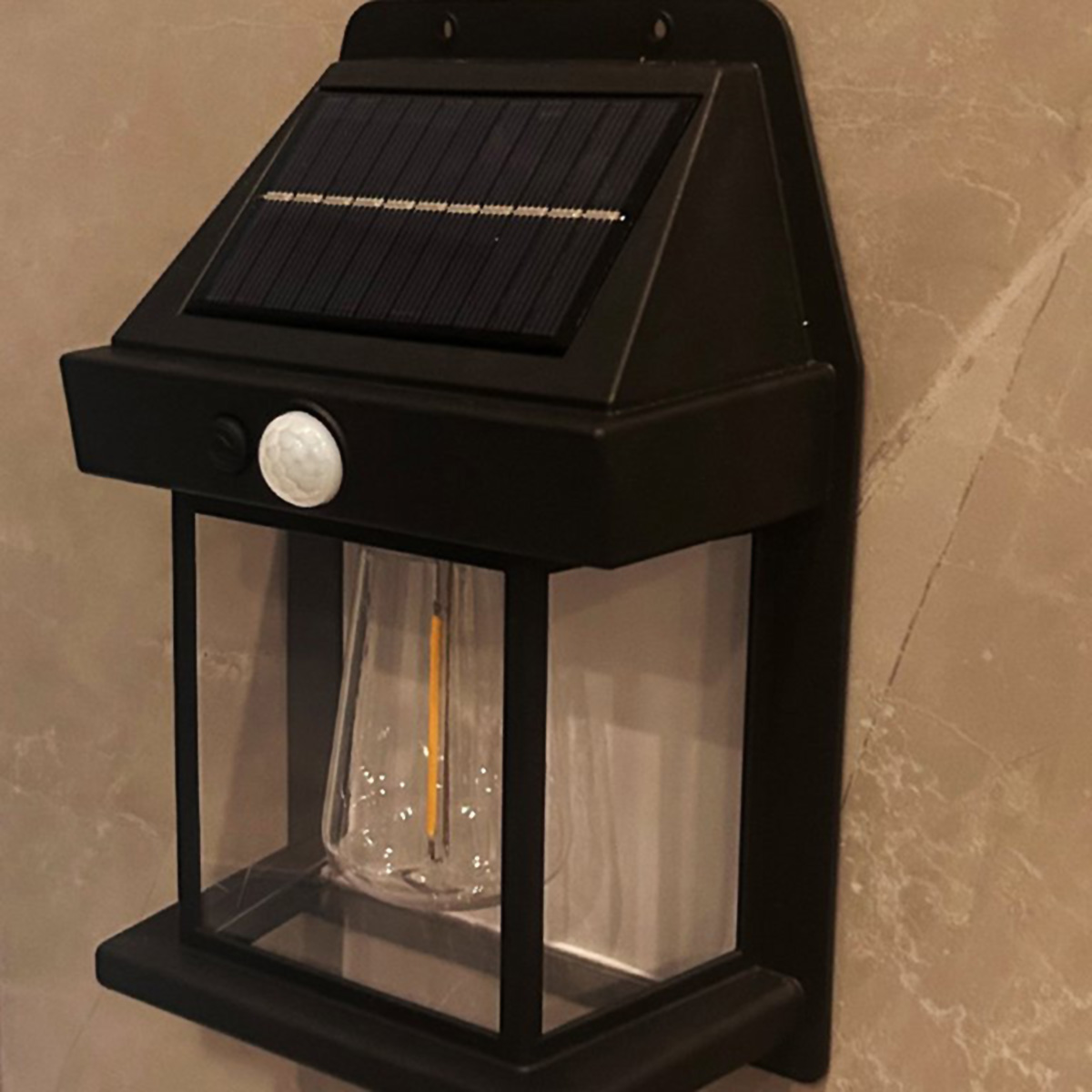 Lámpara de pared negra con energía solar, con una carcasa de vidrio transparente, montada en pared beige.