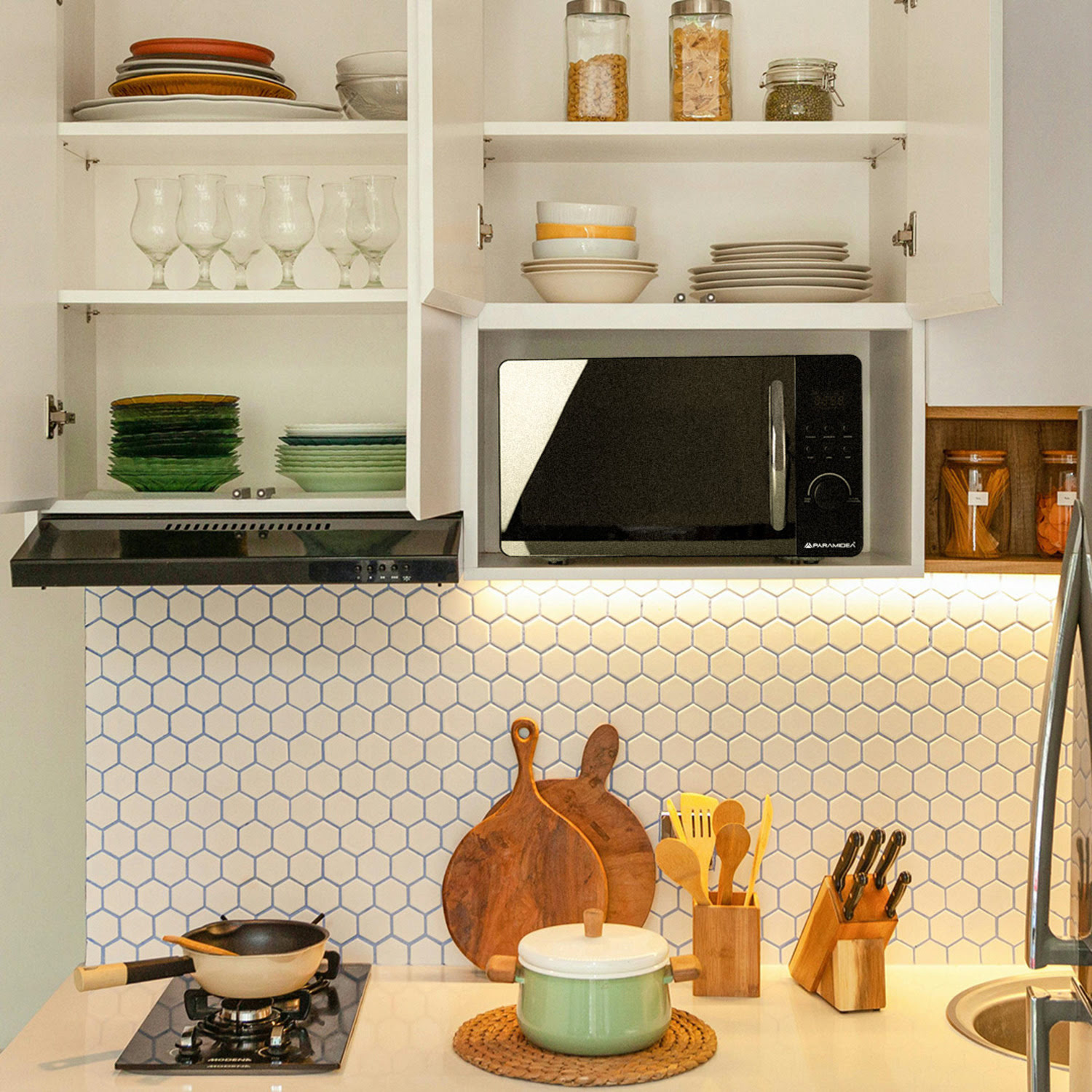 Scena di cucina con microonde, fornello e vari utensili da cucina.