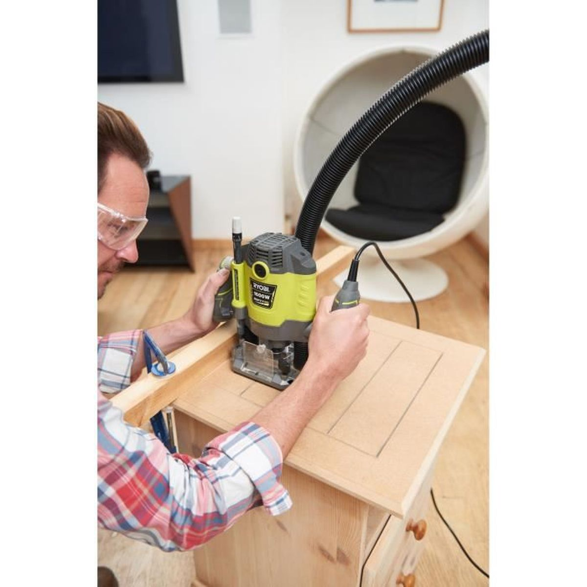 Ein Mann benutzt eine Oberfräse an einem Holzschrank. Er trägt eine Schutzbrille.