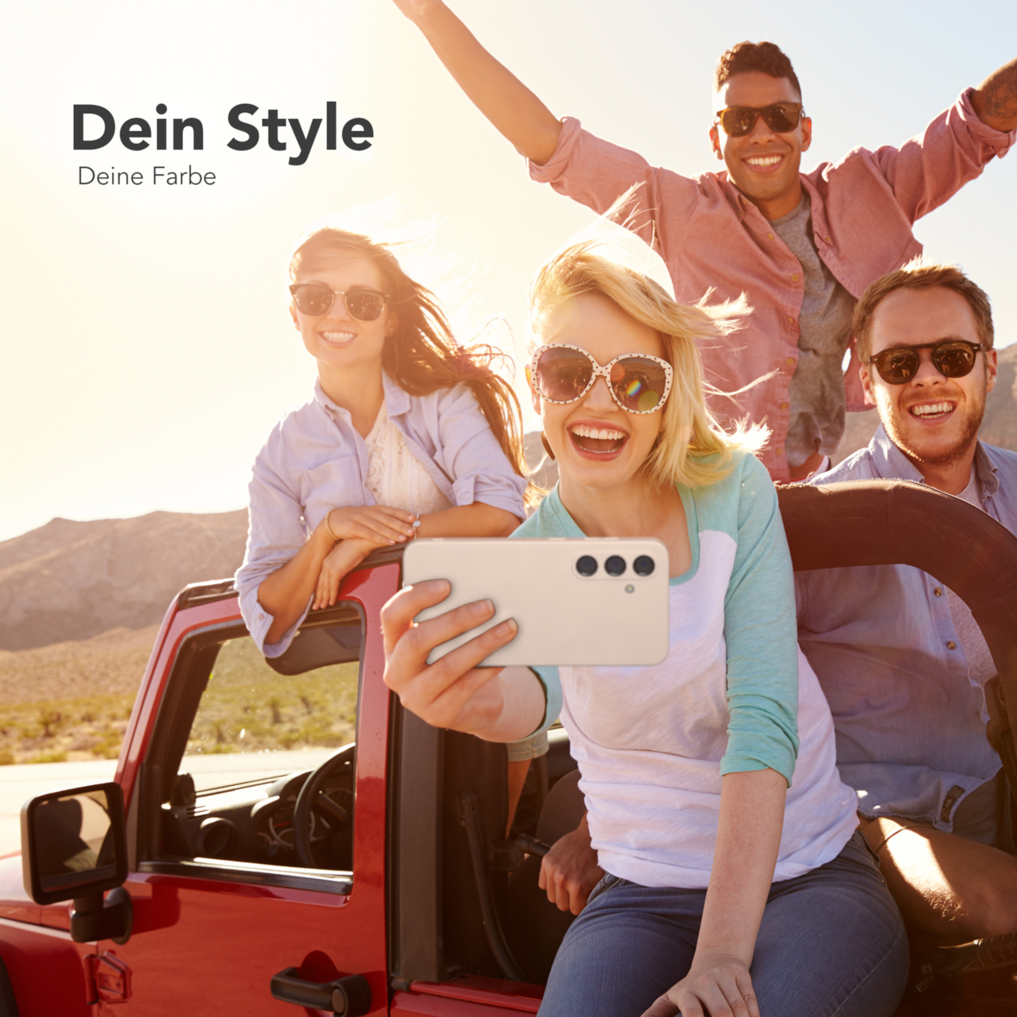 Vier Personen machen ein Selfie in einem roten Jeep. Die Sonne scheint und sie lächeln.