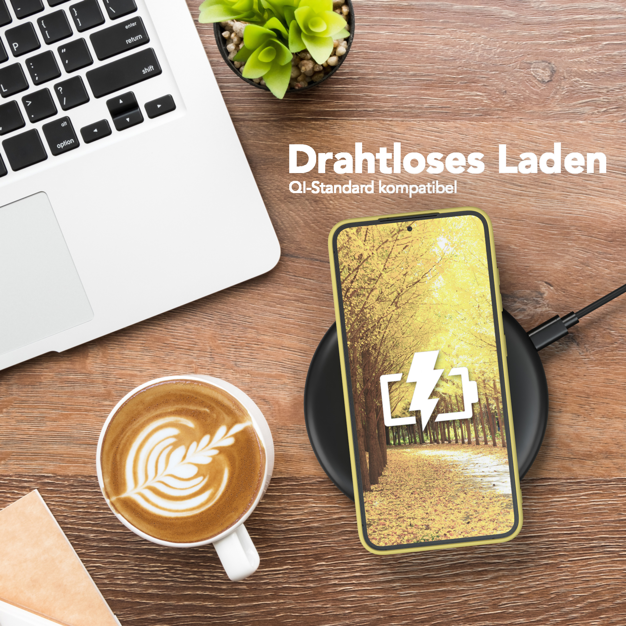 Ein Telefon mit Ladesymbol auf einem Ladepad, neben Kaffee und einem Laptop.