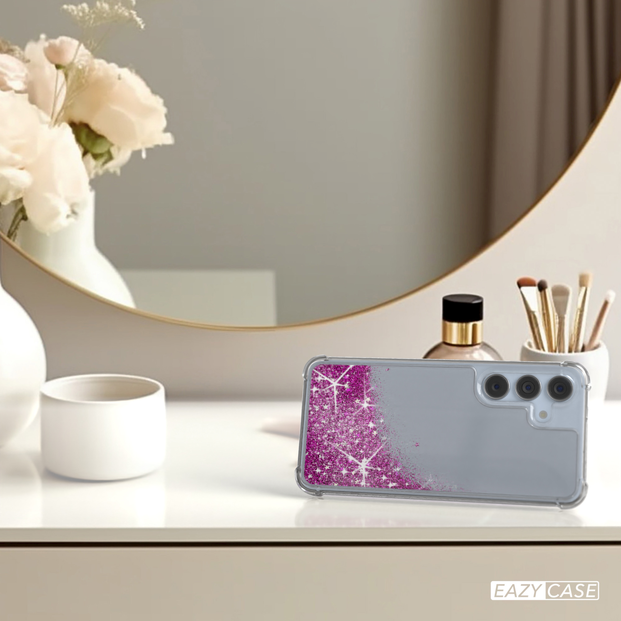 Handyhülle mit rosa Glitzer in Flüssigkeit, auf einem Tisch, neben Spiegel und Blumen.