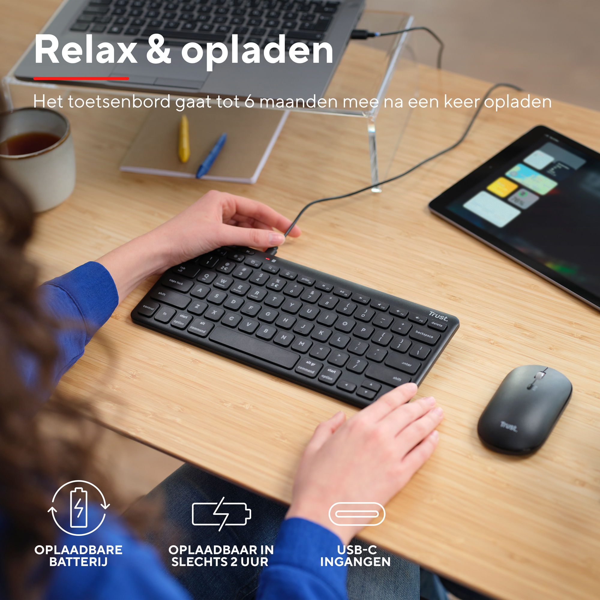 Osoba używająca czarnej klawiatury i myszy na drewnianym biurku z tabletem i kubkiem.