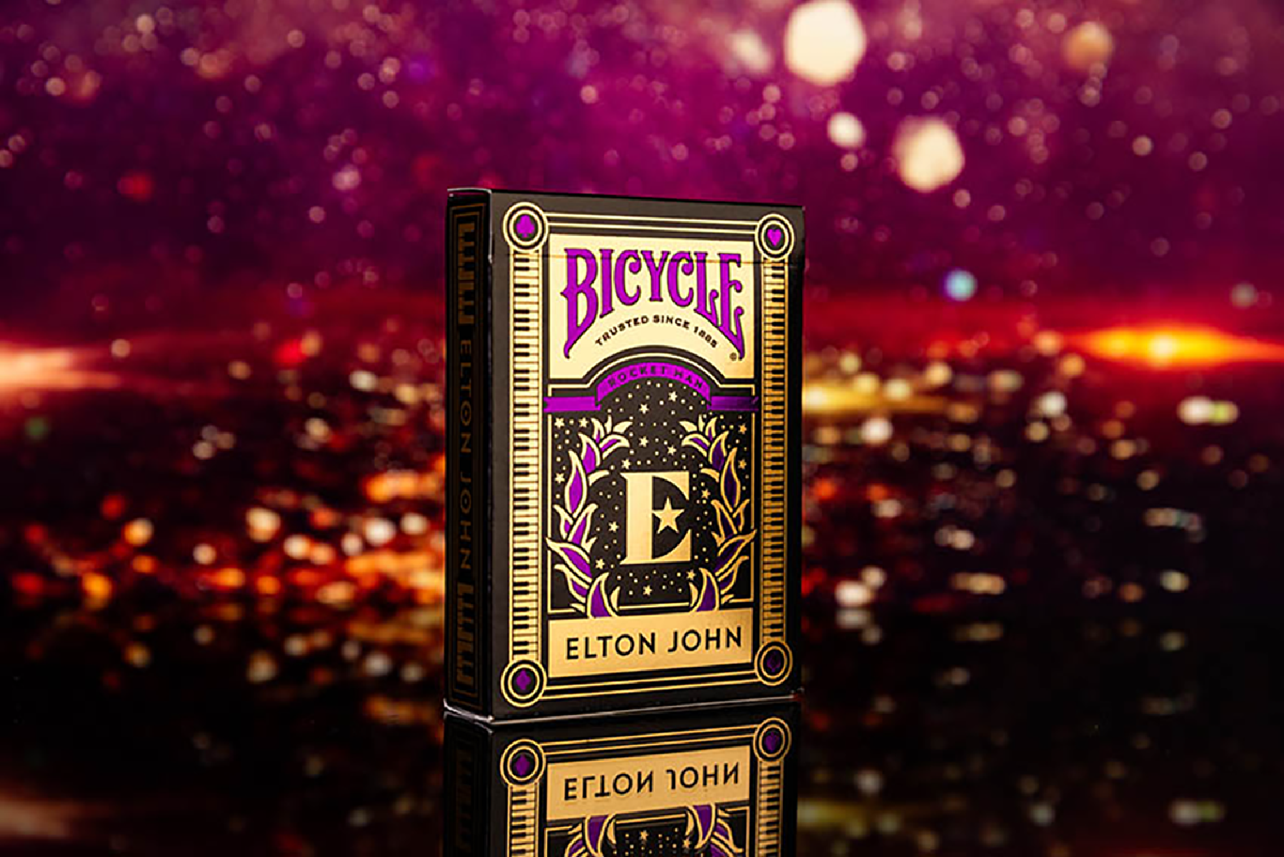 Kartenspiel Bicycle Elton John. Schwarze Box mit goldenen Akzenten, vor verschwommenem Stadt-Hintergrund.