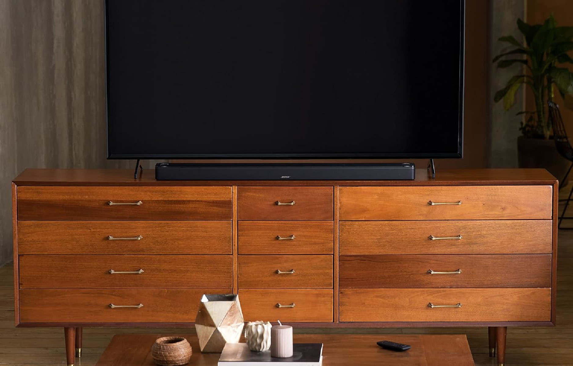 Ein Holzschrank mit einer schwarzen Soundbar und einem großen schwarzen Fernseher, beiger Hintergrund.