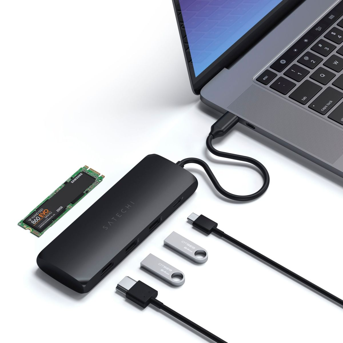 Laptop mit schwarzem Hub verbunden, mit SSD, USB-Laufwerken und Kabeln auf weißer Oberfläche.