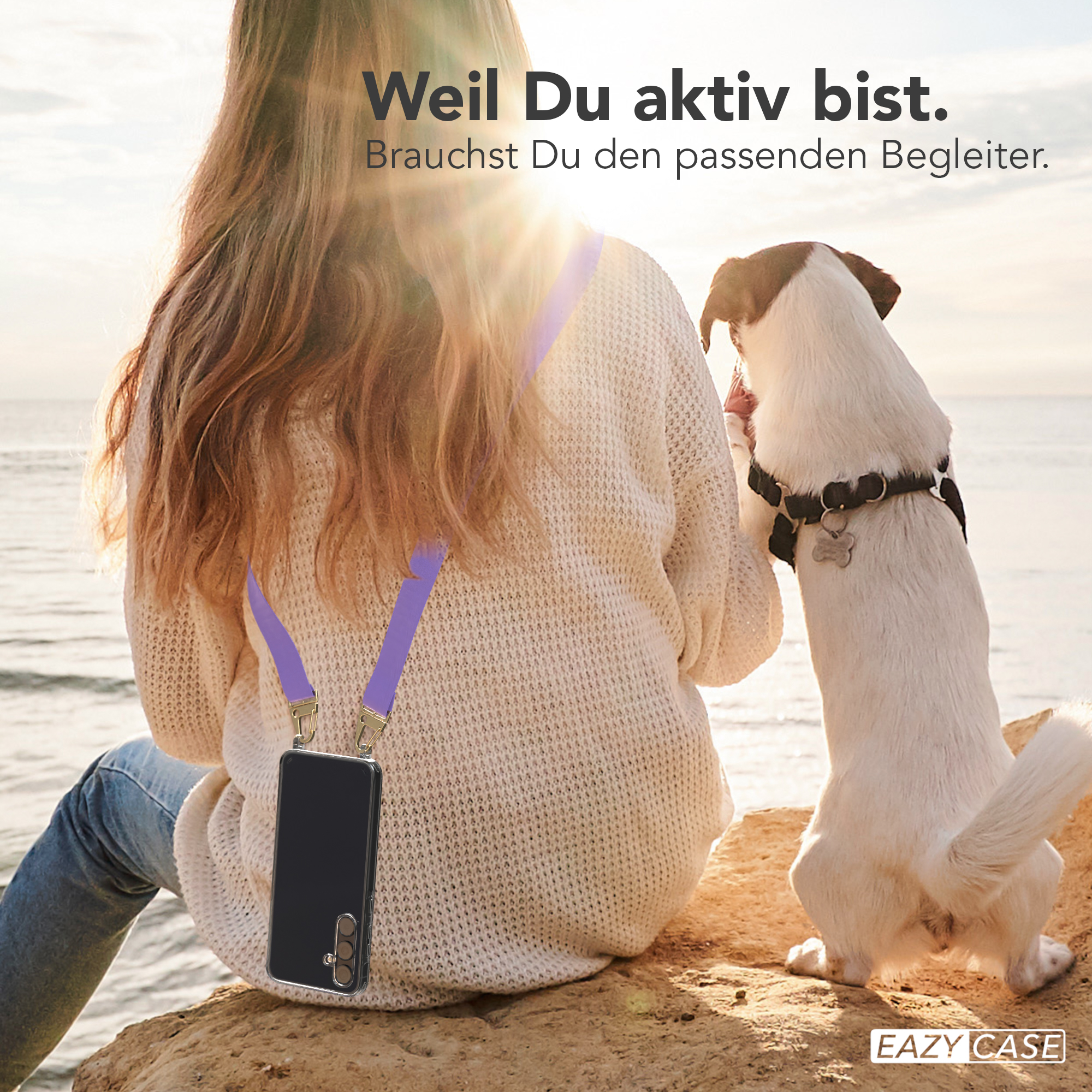 Frau mit Handy an der Leine am Strand mit Hund. Der Hund schaut sie an.