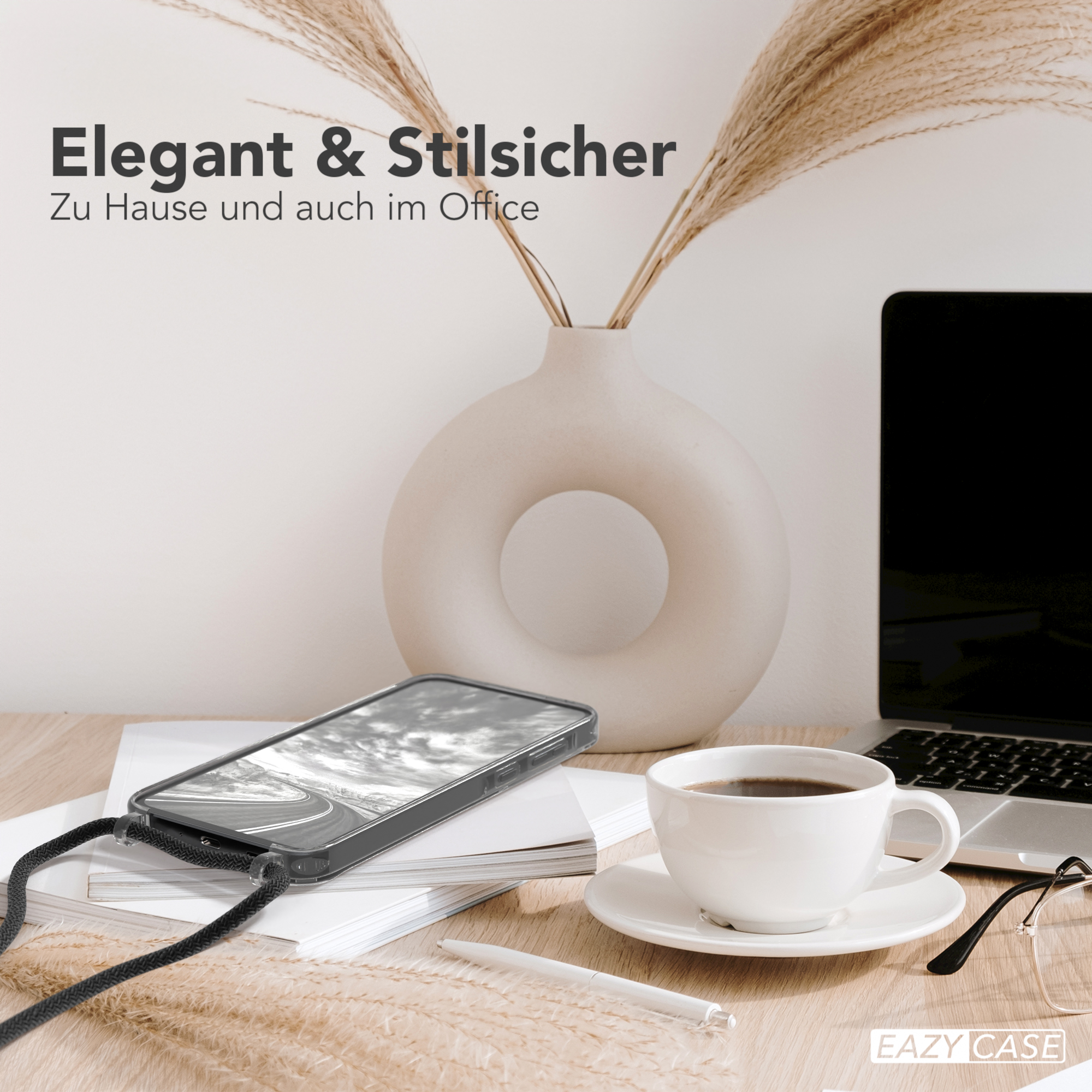 Ein Telefon mit schwarzer Hülle und einem Trageriemen auf einem Schreibtisch mit Kaffeetasse und Brille.